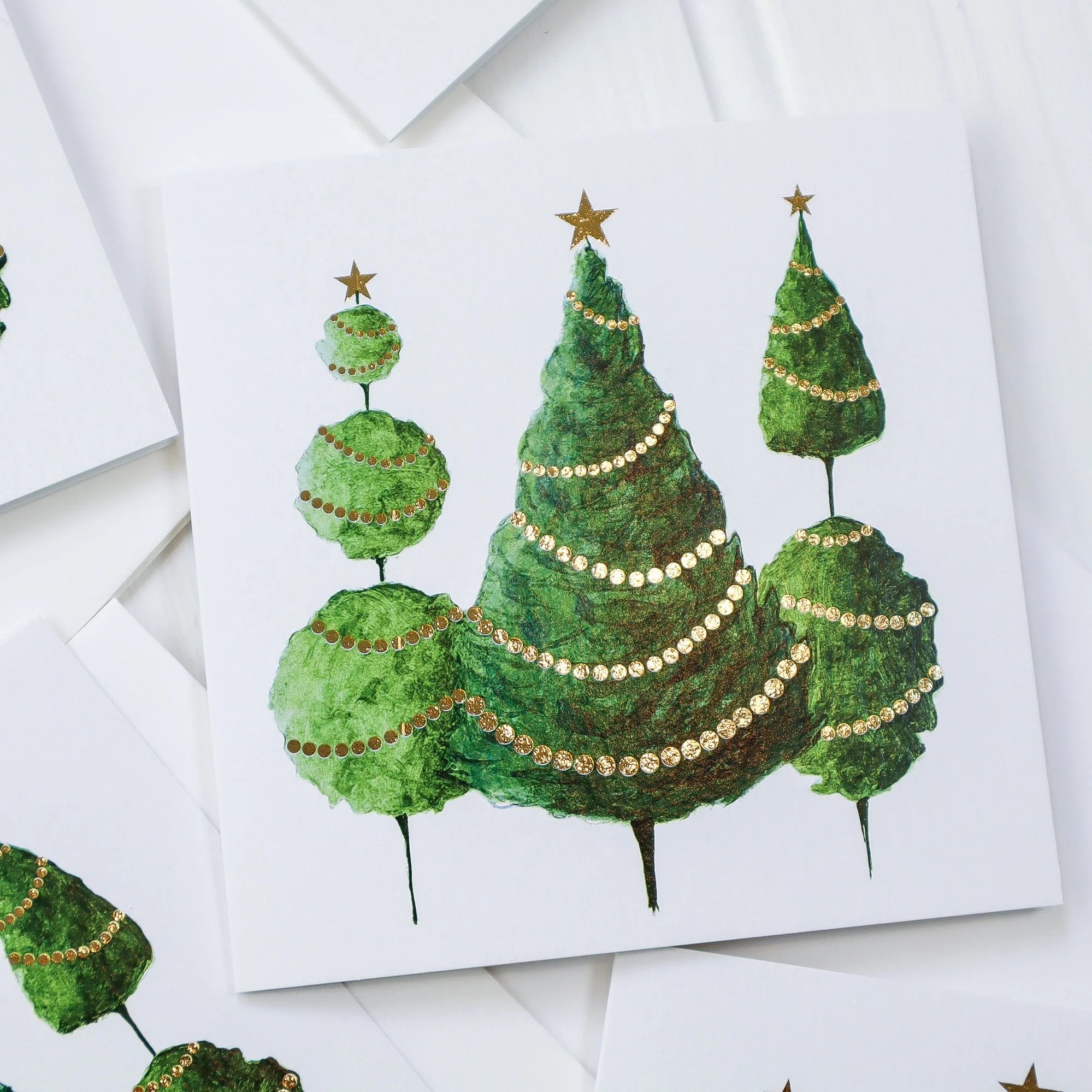 Aerial view of a recycled luxury Christmas card featuring three hand painted trees and golden fairy lights.
