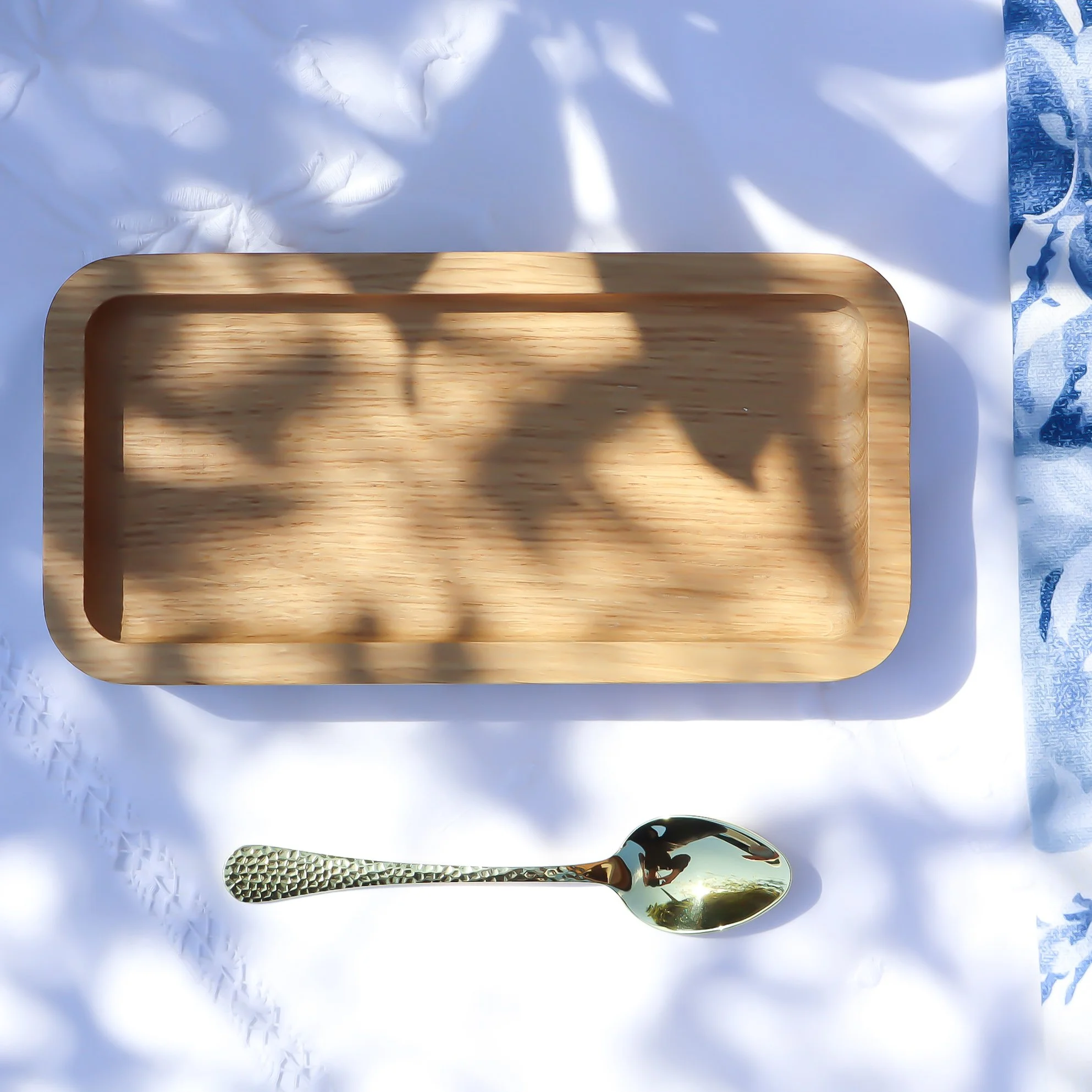 Aerial view of a sustainable PEFC oak teatime tray made in the West Country. The tray sits on a white embroidered tablecloth and golden teaspoon.