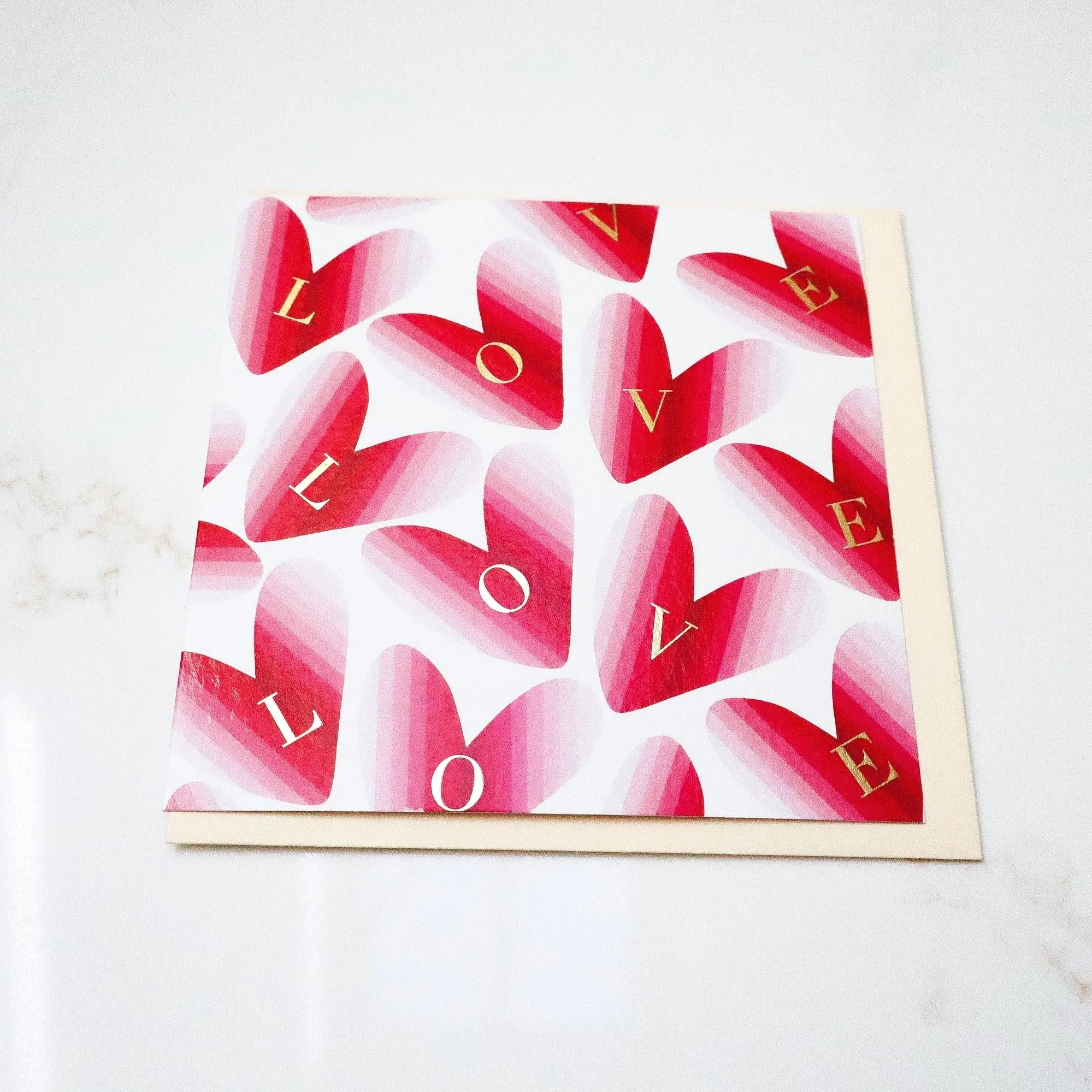 An aerial photo of a greeting card featuring hand painted red hearts with gold foil letters reading LOVE.
