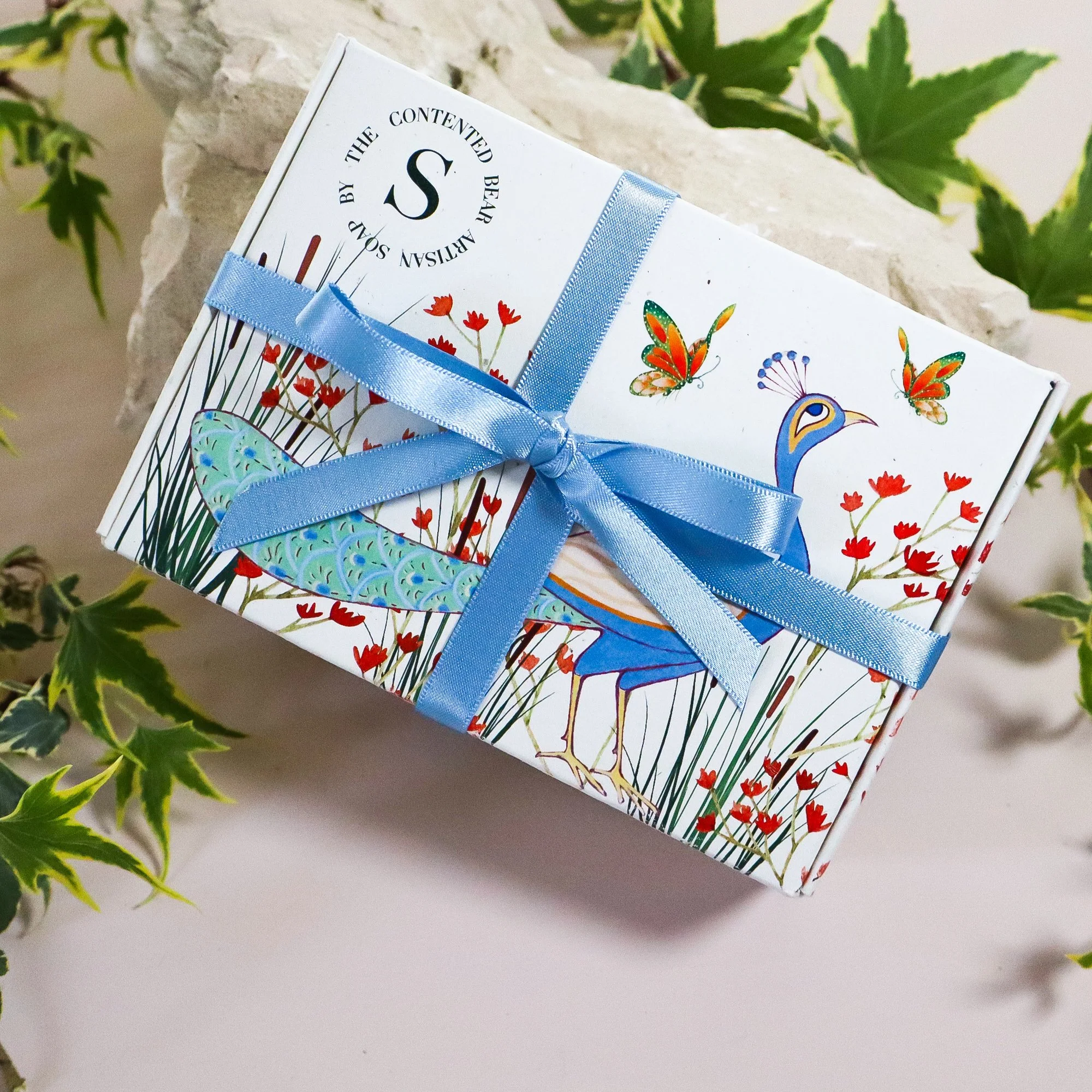 Flat lay of a beautufl illustrated soap bow featuring a peacock with sustainable, recycled ribbon wrapped around the soap box and ivy dotted around the box.