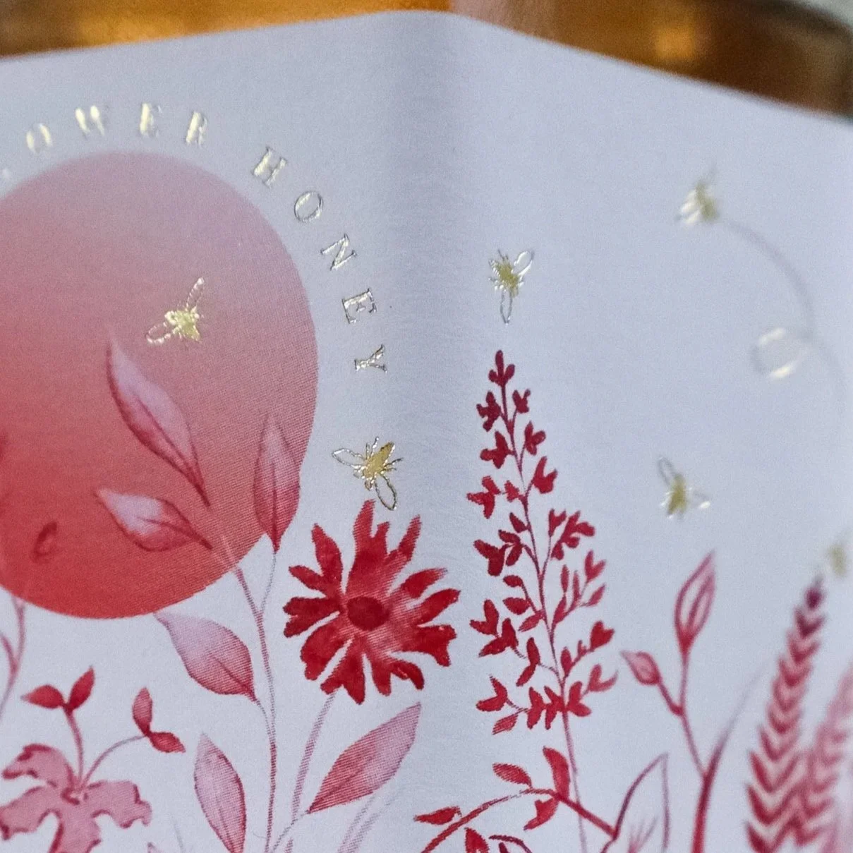 Close-up of a stunning luxury, hand illustrated honey label with red flowers and gold foil honeybees.