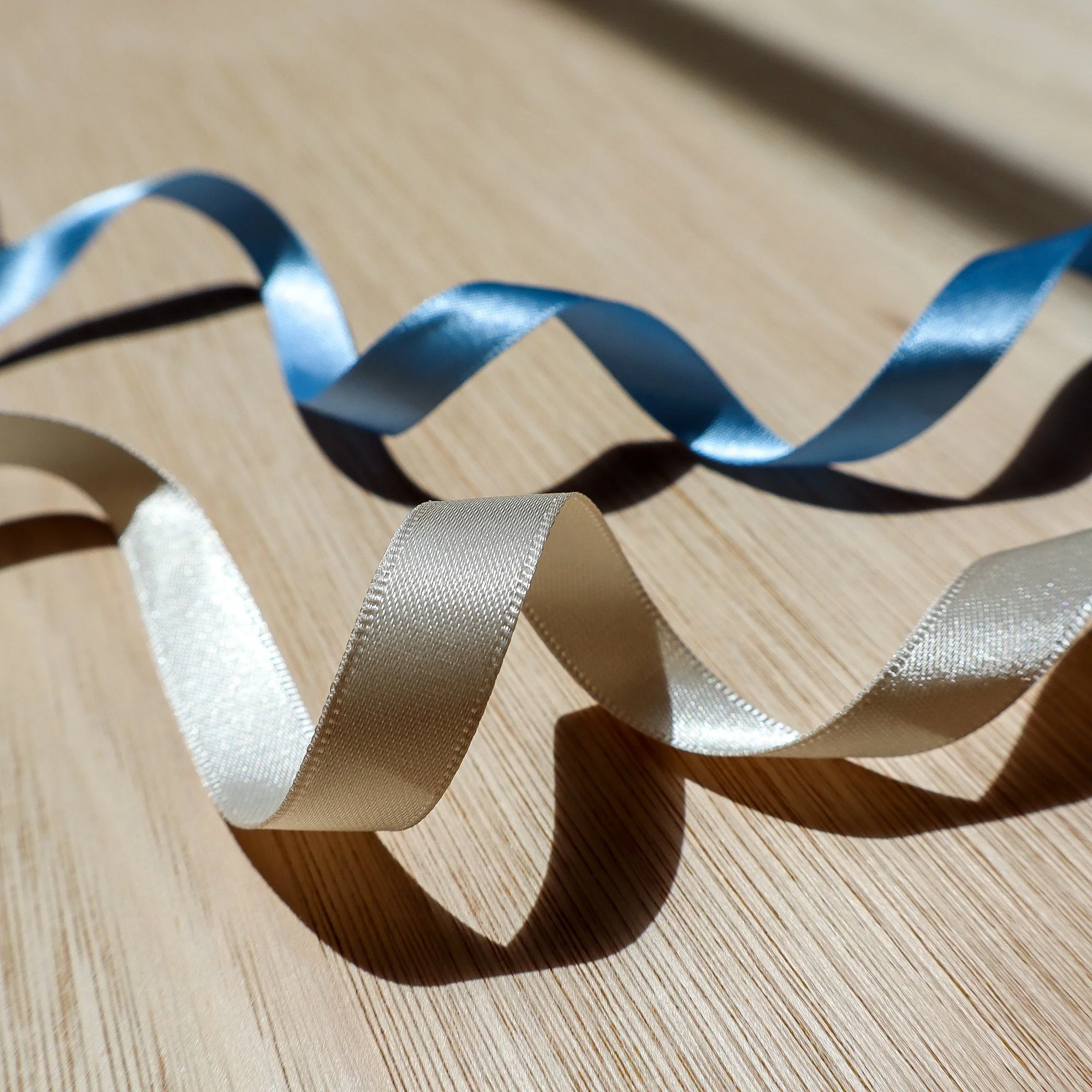 A close up of two curled ribbons one in ivory and one in wedgewood blue, both made from recycled plastic PET bottles.