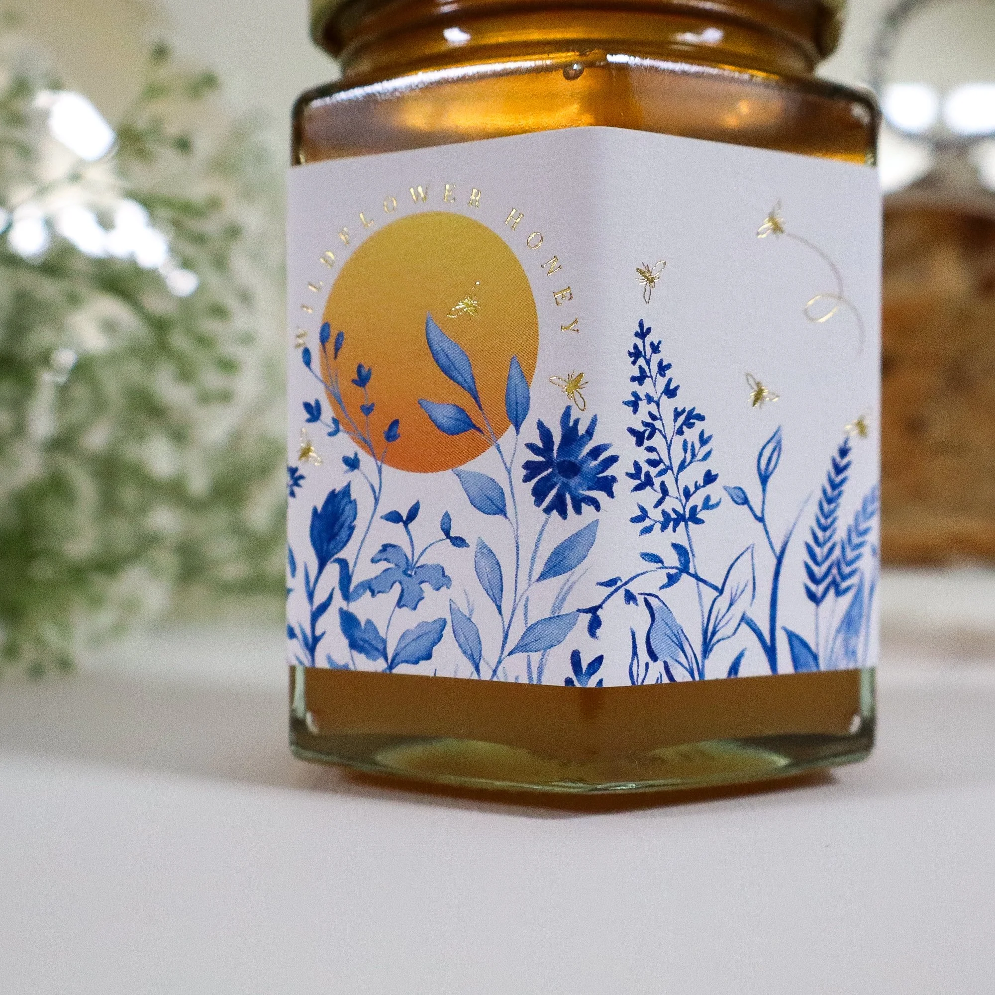A close-up view of a beautiful, illustrated honey label with blue meadow and yellow sun. Details of gold foil honeybees are on the label.
