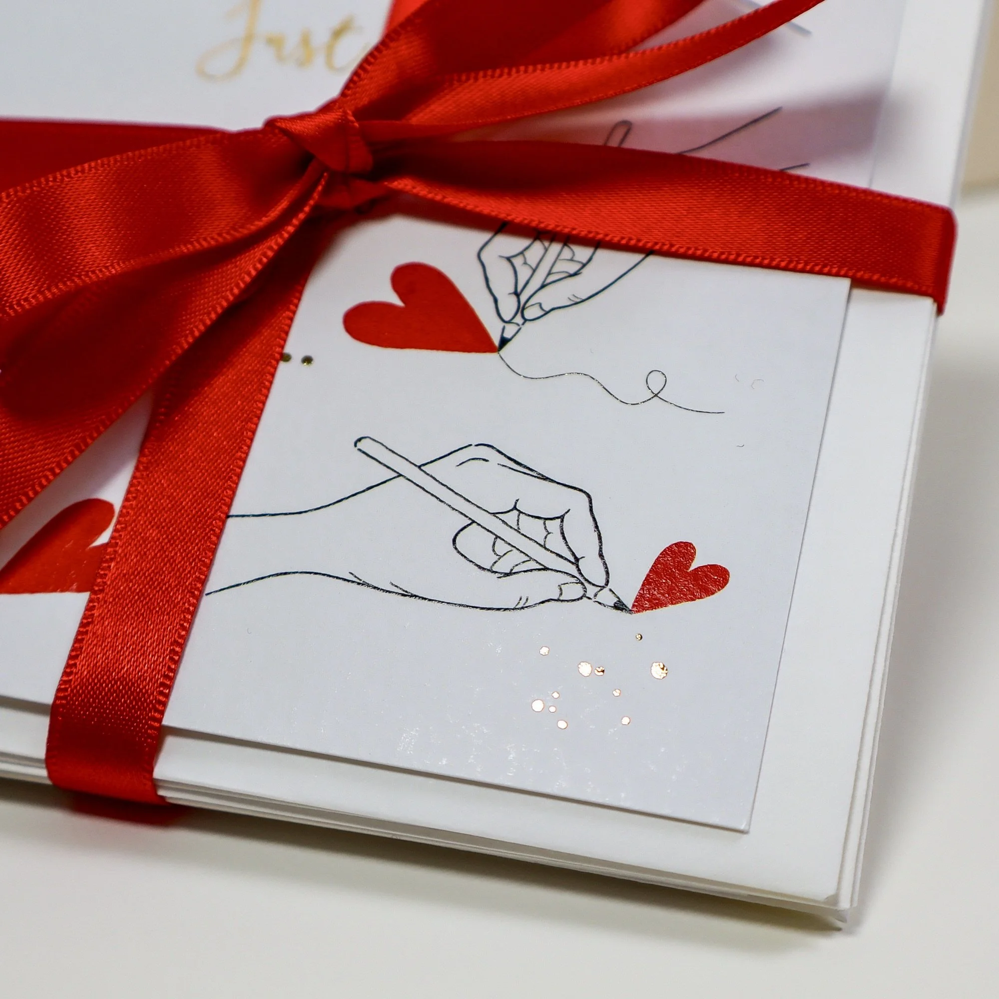 A close up view showing a hand drawn hand drawing a red heart with gold foil ink spots glinting in the light.