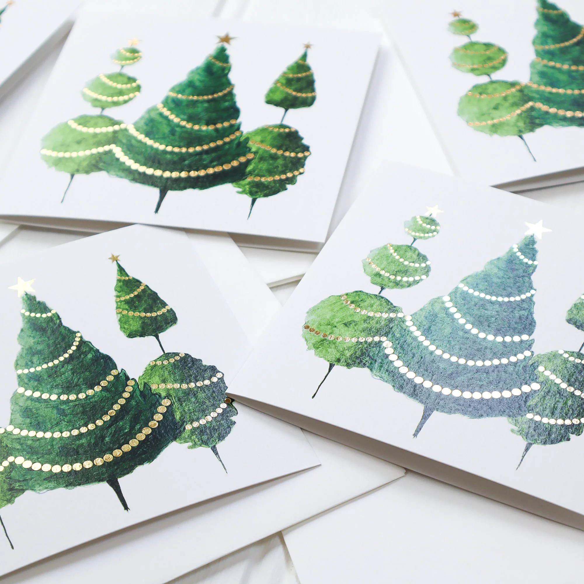 An aerial view of three eco Christmas cards featuring three hand illustrated Christmas trees with gold fairy lights.