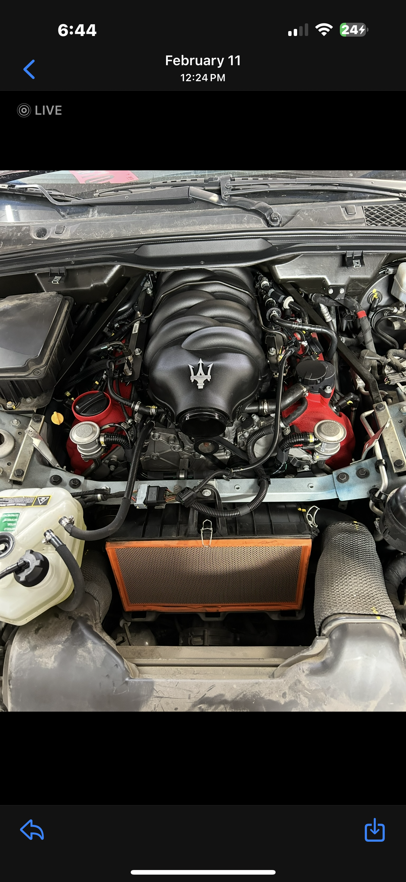Car engine with a black hood ornament featuring the Maserati trident logo, surrounded by various engine components.