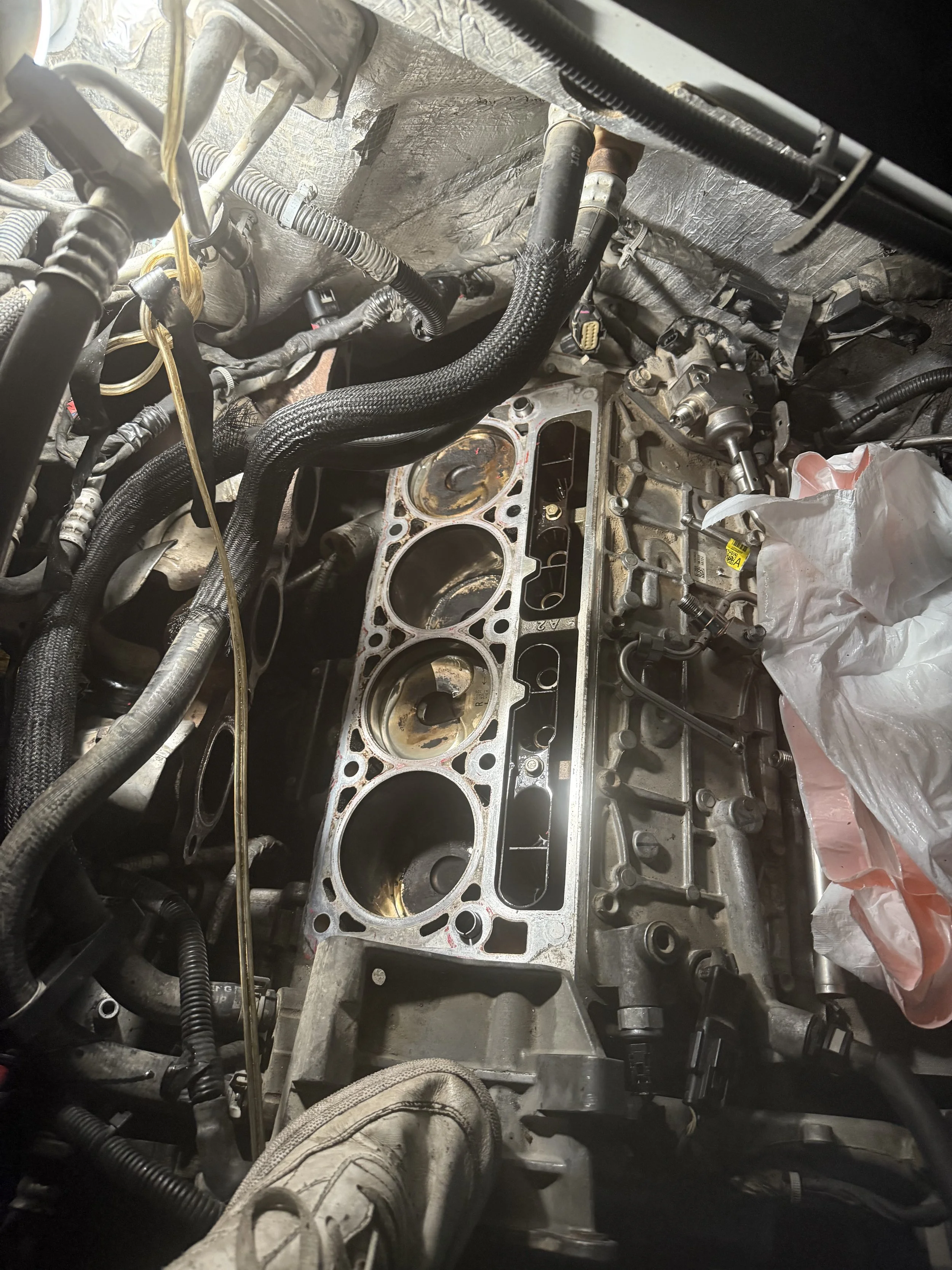 An engine with the cylinder head removed exposing the cylinders and pistons, with various engine components and hoses surrounding it.