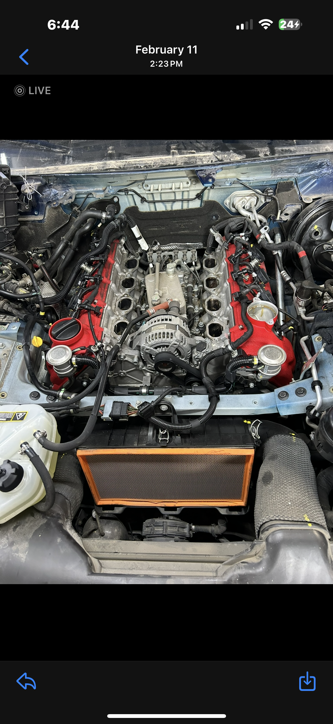 Car engine bay with the engine removed, exposing internal components and wiring, with a radiator and coolant reservoir visible.