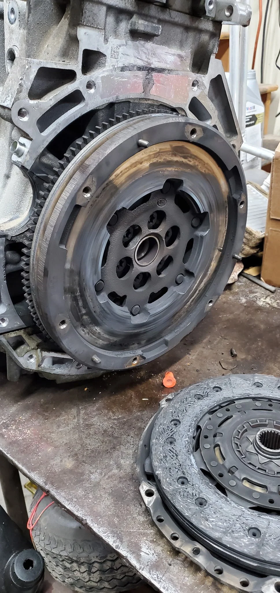 Disassembled engine components on a metal workbench, including a large engine flywheel and pressure plate paired together.