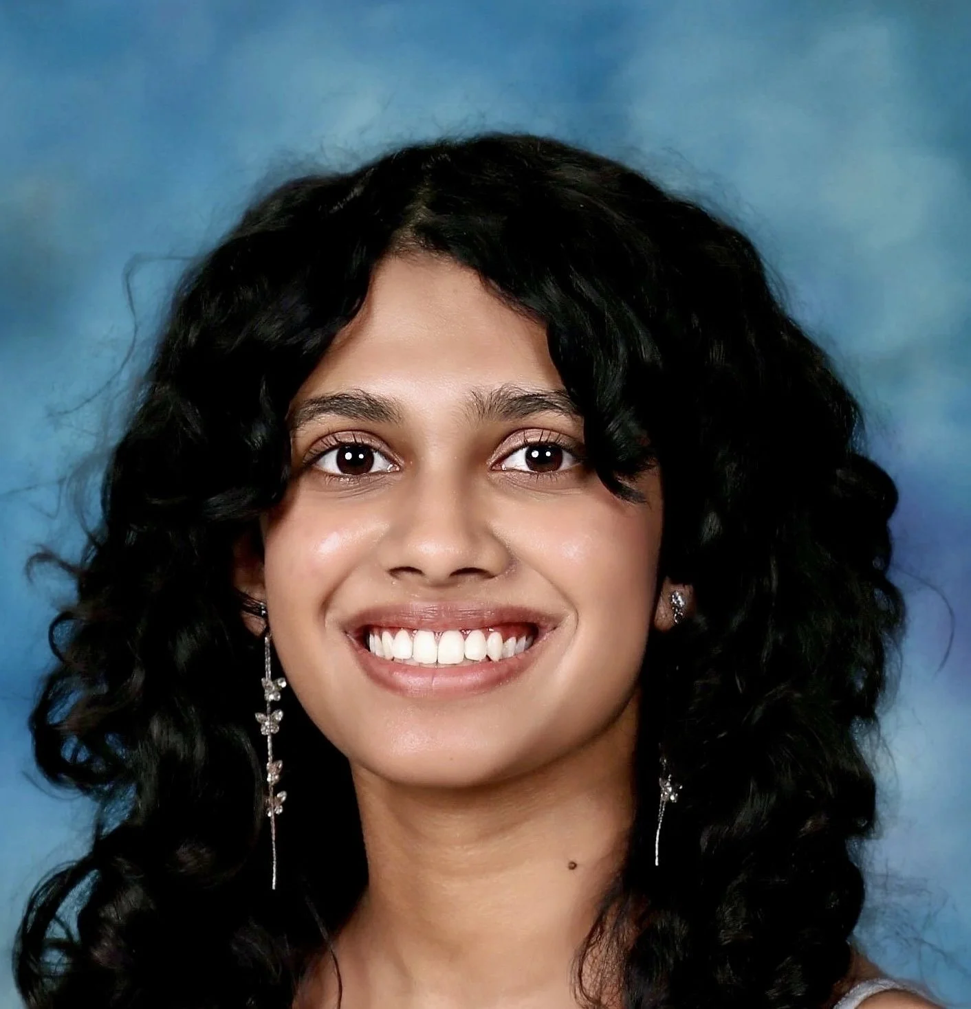 Close-up portrait of a woman with curly black hair, brown eyes, and a bright smile, against a blue background.