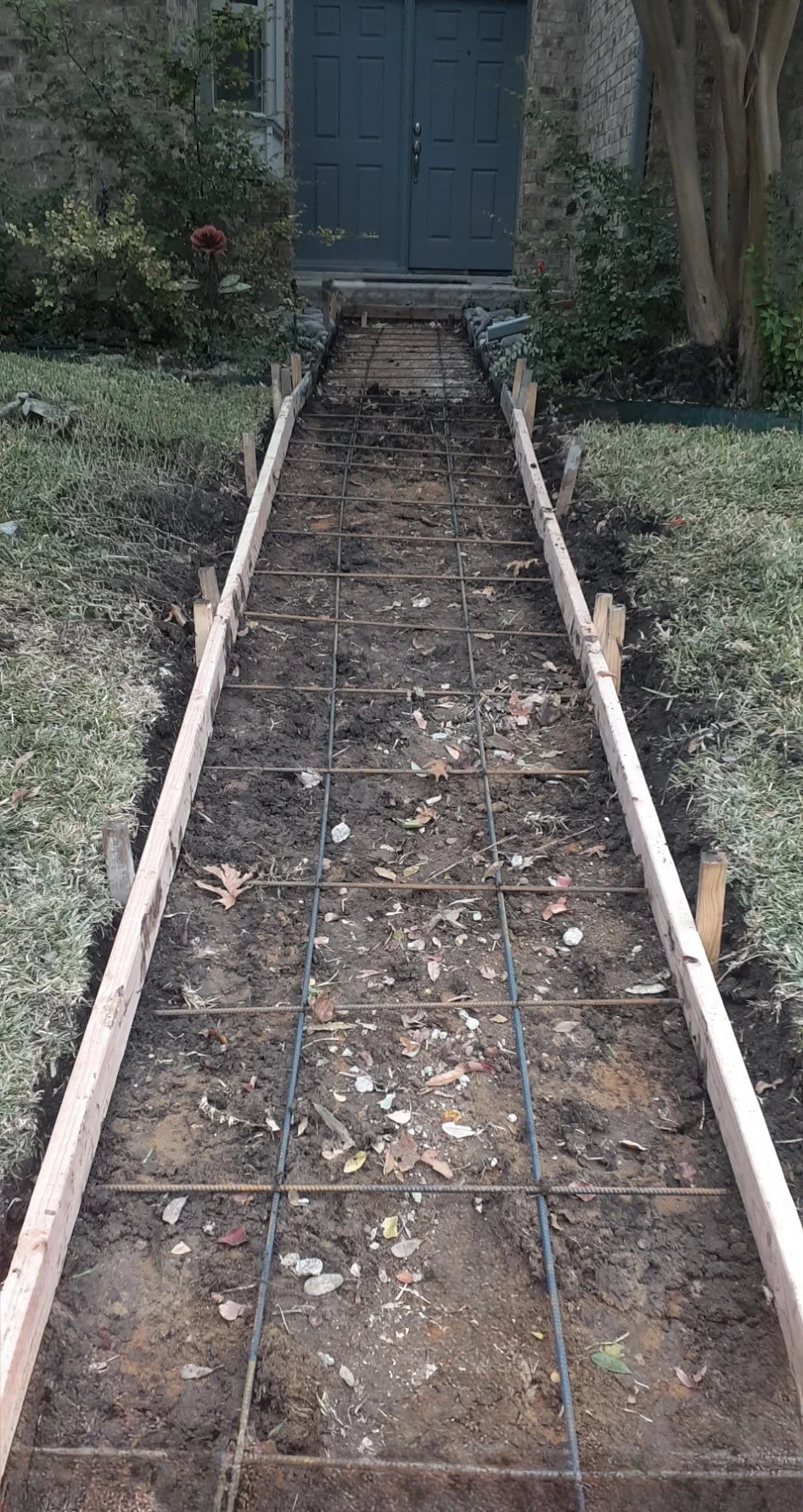 A pathway under construction leading up to a blue door, with wooden framing and rebar in the ground.