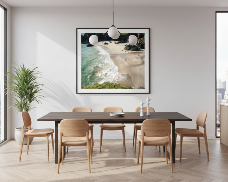Modern dining room with a dark wood table, six wooden chairs, a framed beach photograph on the wall, a pendant light fixture, a large window, and a potted plant.
