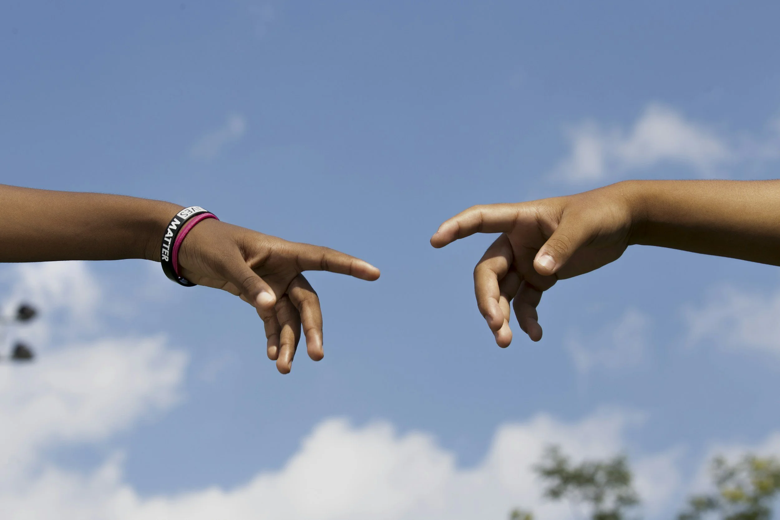Two hands reaching towards each other with index fingers extended, inspired by Michelangelo's The Creation of Adam, against a blue sky background.