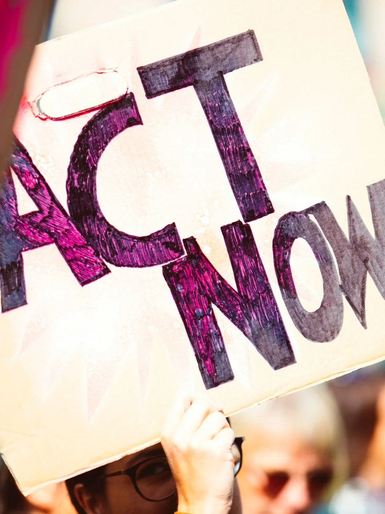 Person holding sign that says 'ACT NOW' at a protest or rally.