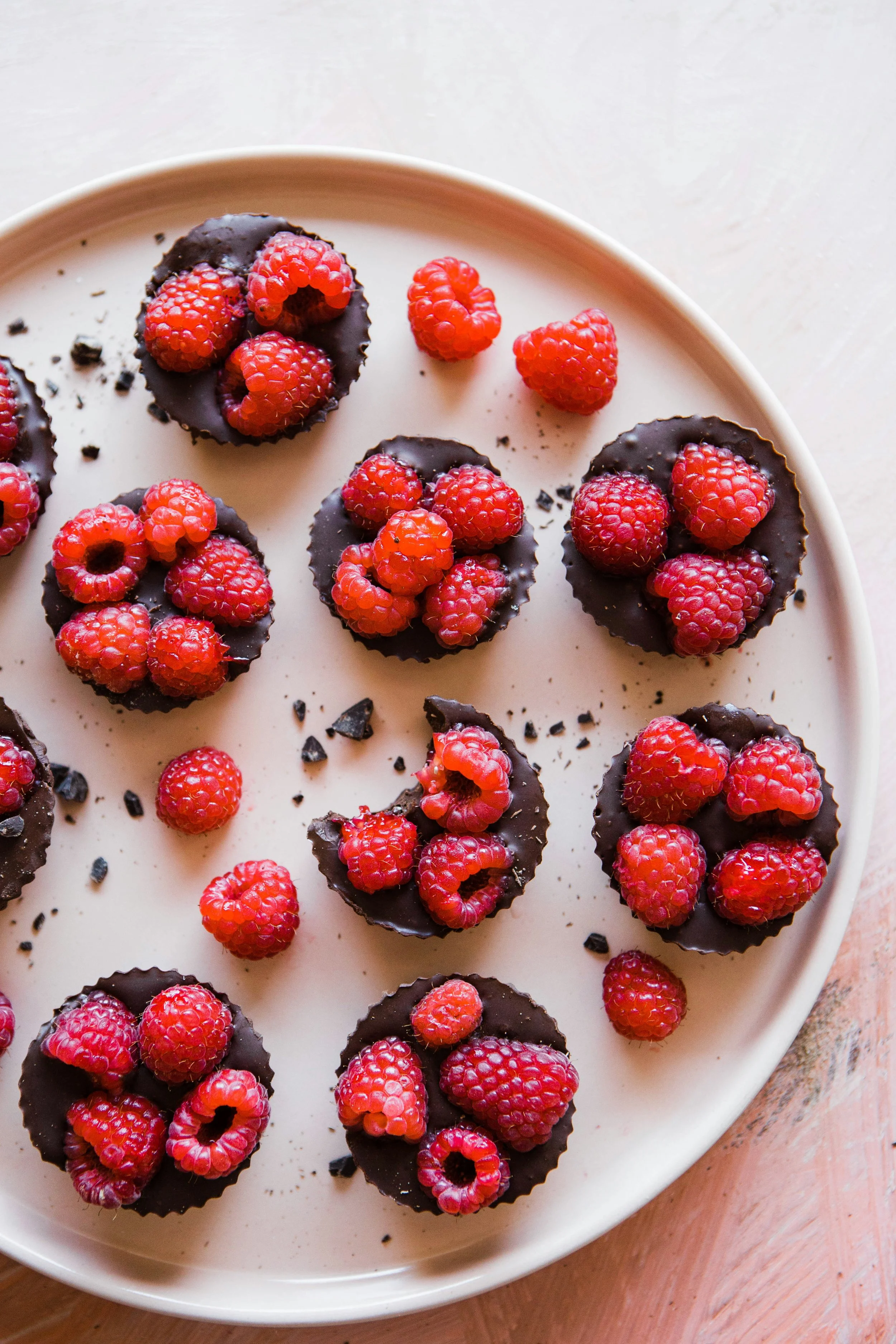 Chocolate cups topped with raspberries on a white plate.