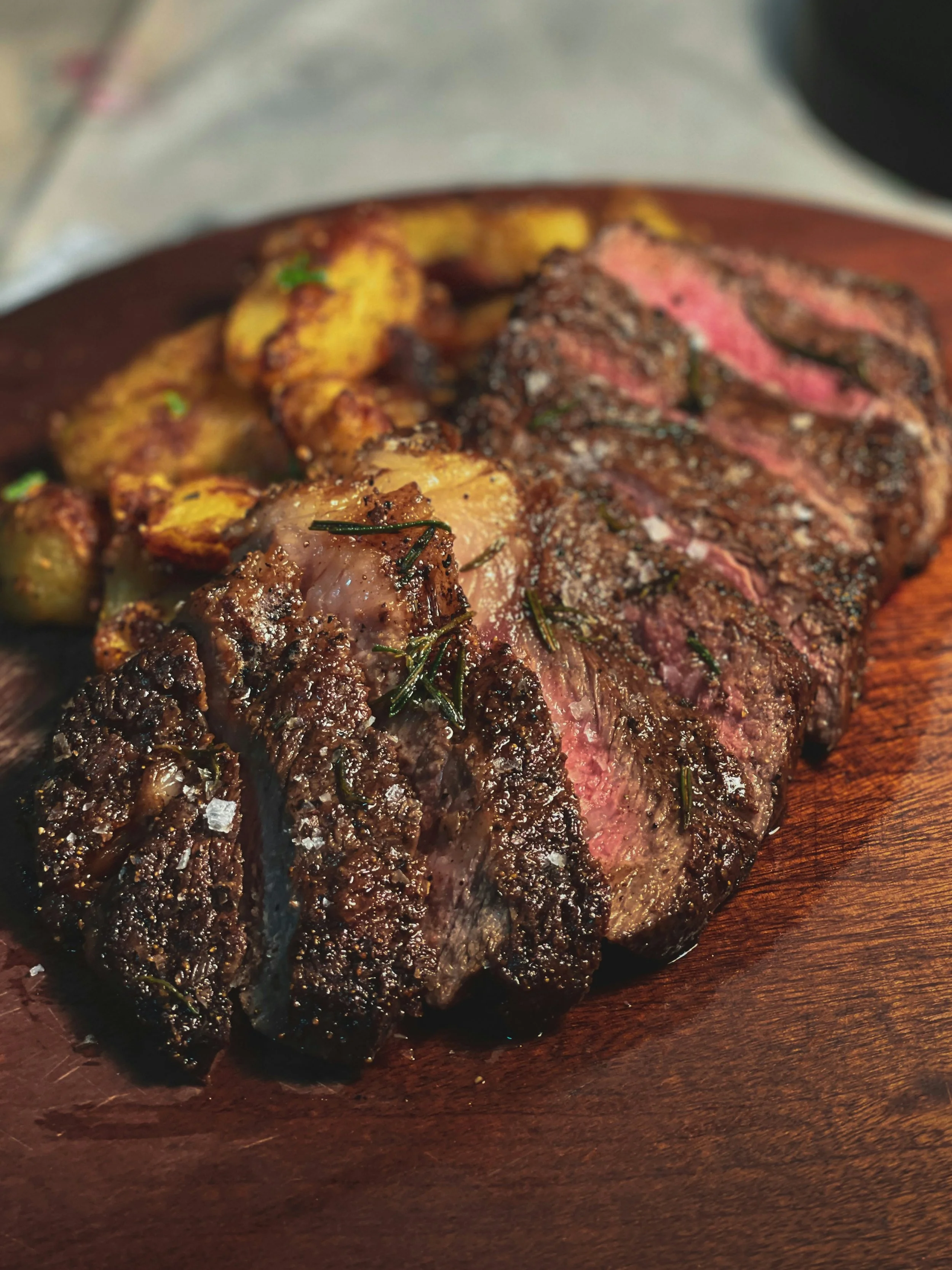 Sliced cooked steak with grilled potatoes on a wooden serving platter.
