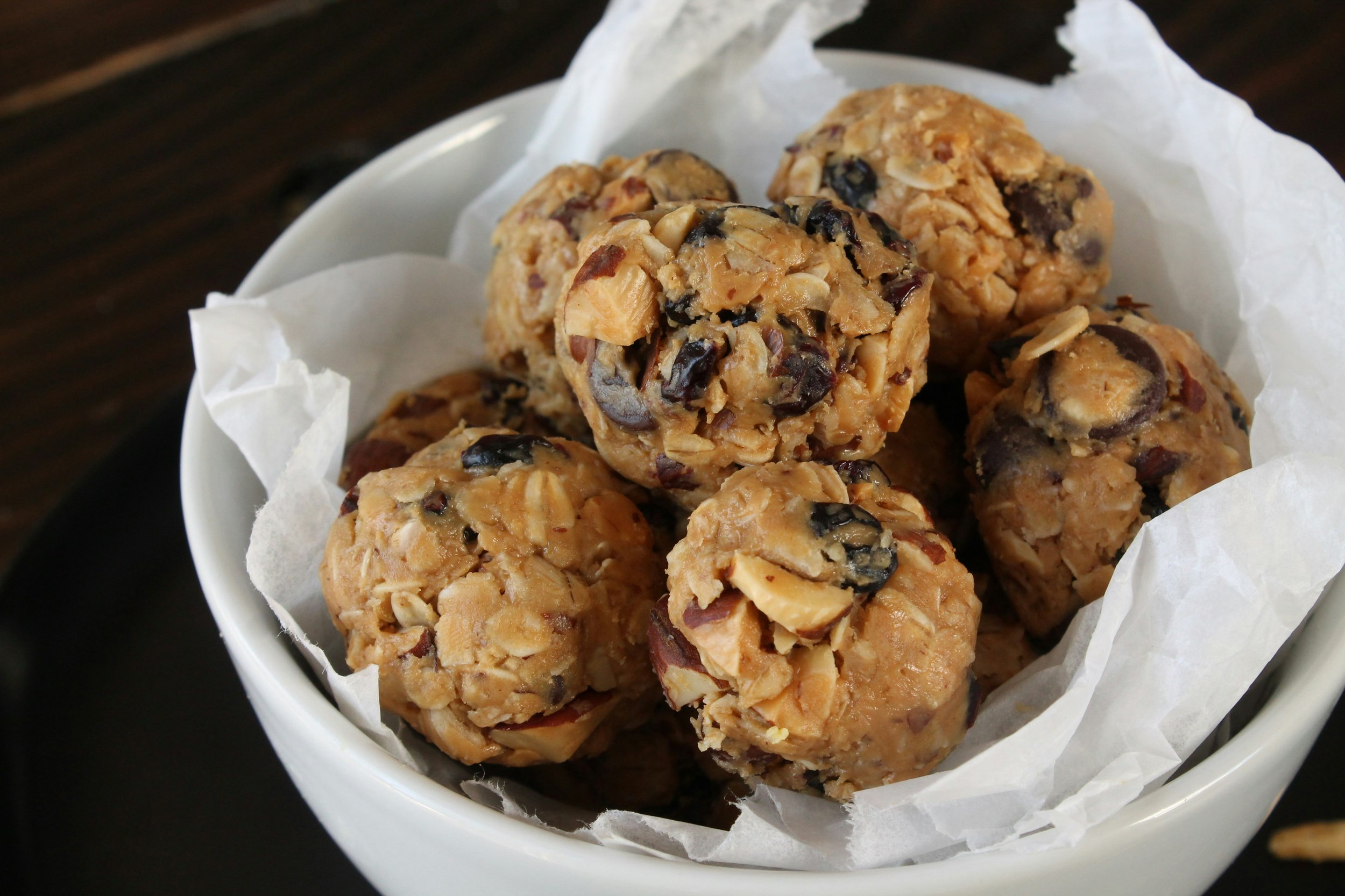 Close-up of oatmeal bite-sized energy balls with oats, nuts, and chocolate chips in a white bowl lined with parchment paper.