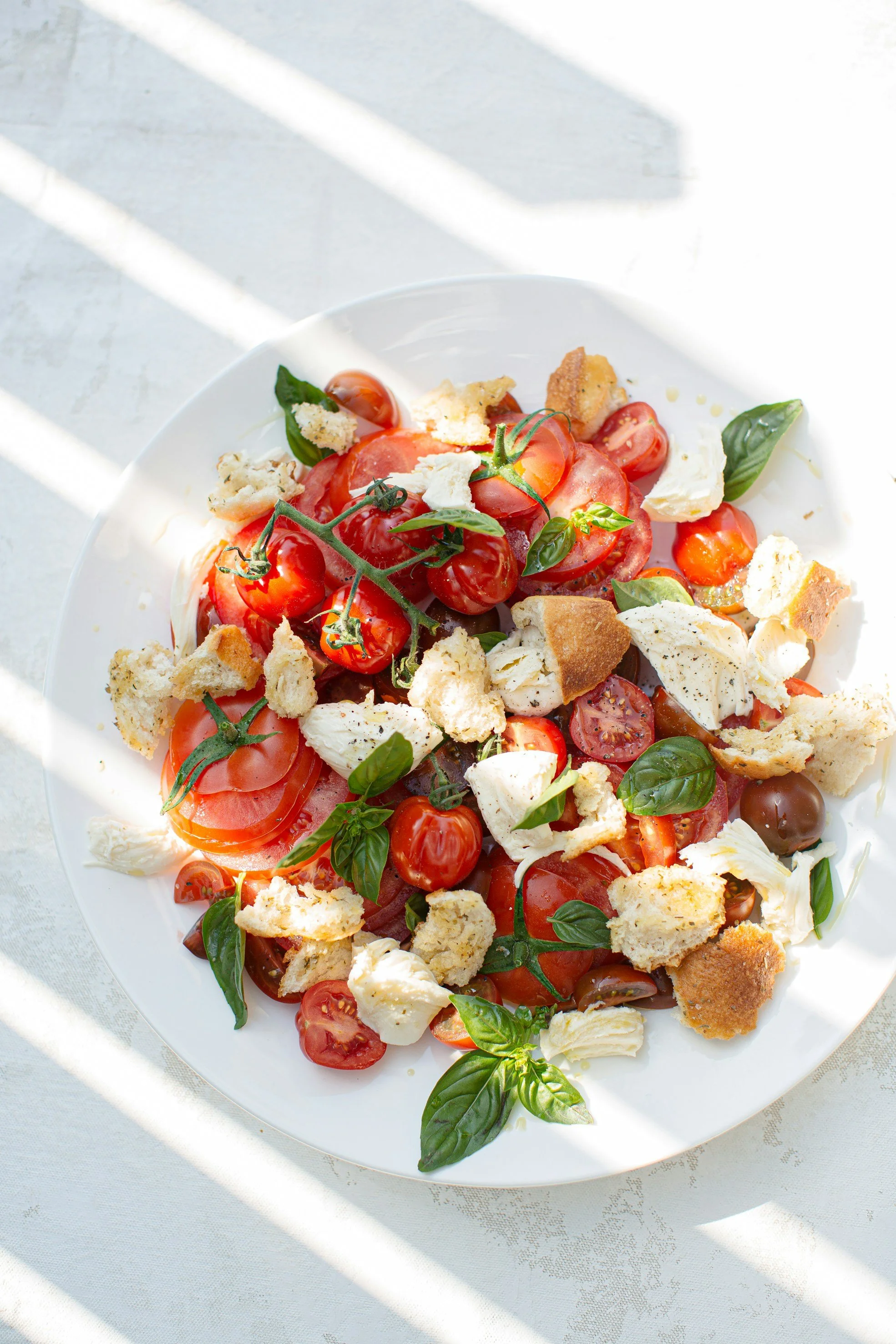 A plate of fresh tomato salad with cherry tomatoes, basil leaves, chunks of mozzarella cheese, and pieces of toasted bread.
