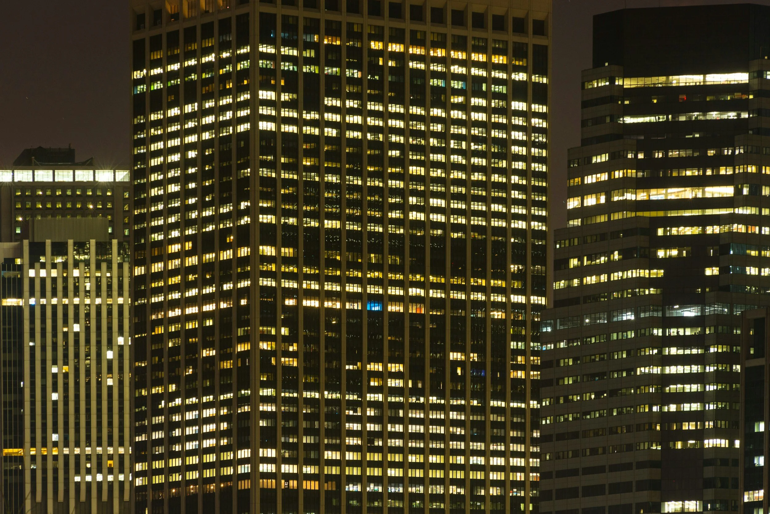 Night view of illuminated office buildings in a city, with the windows lit up in a grid pattern.