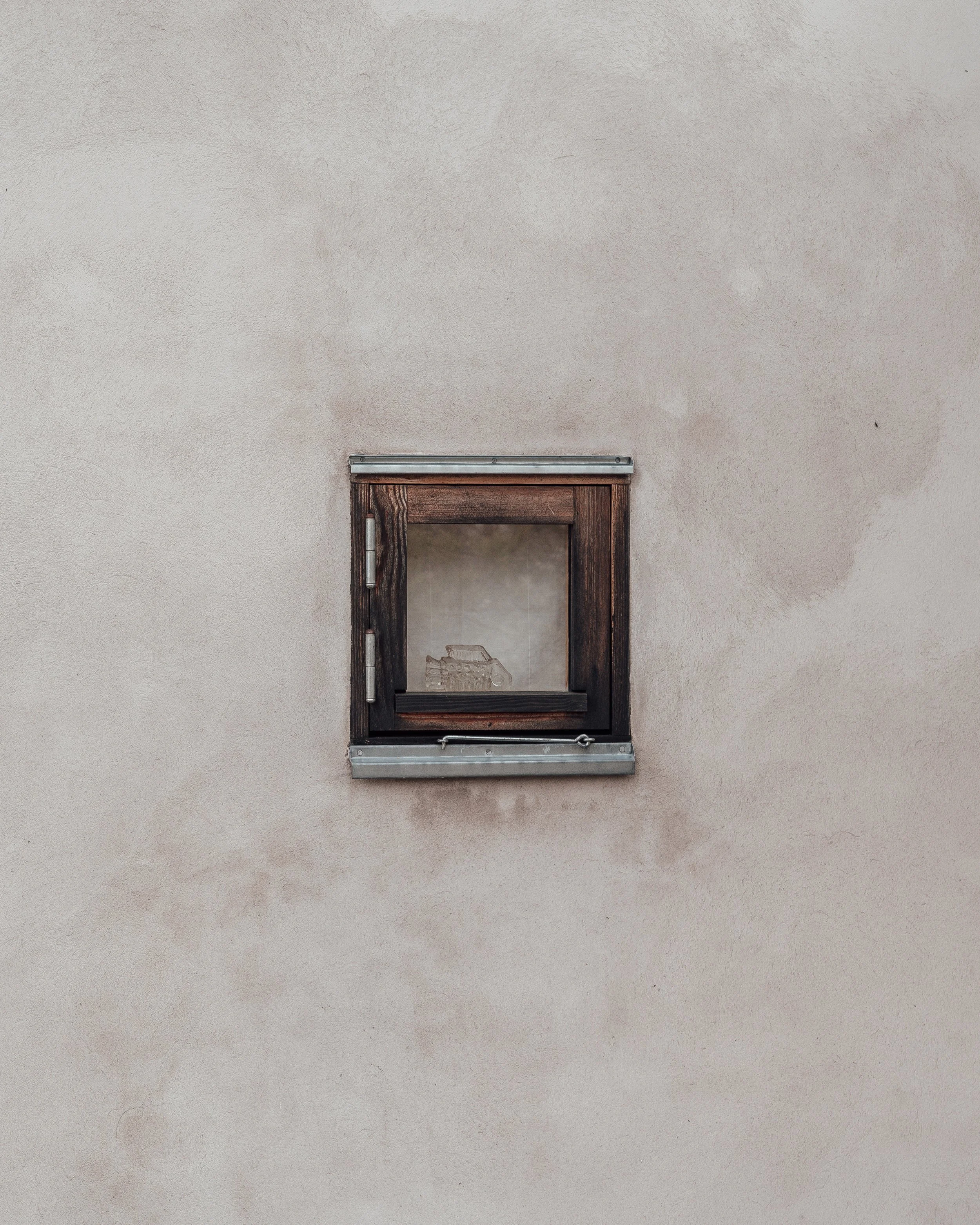 Ett litet fönster i en beige vägg med träram och metallinfattning.