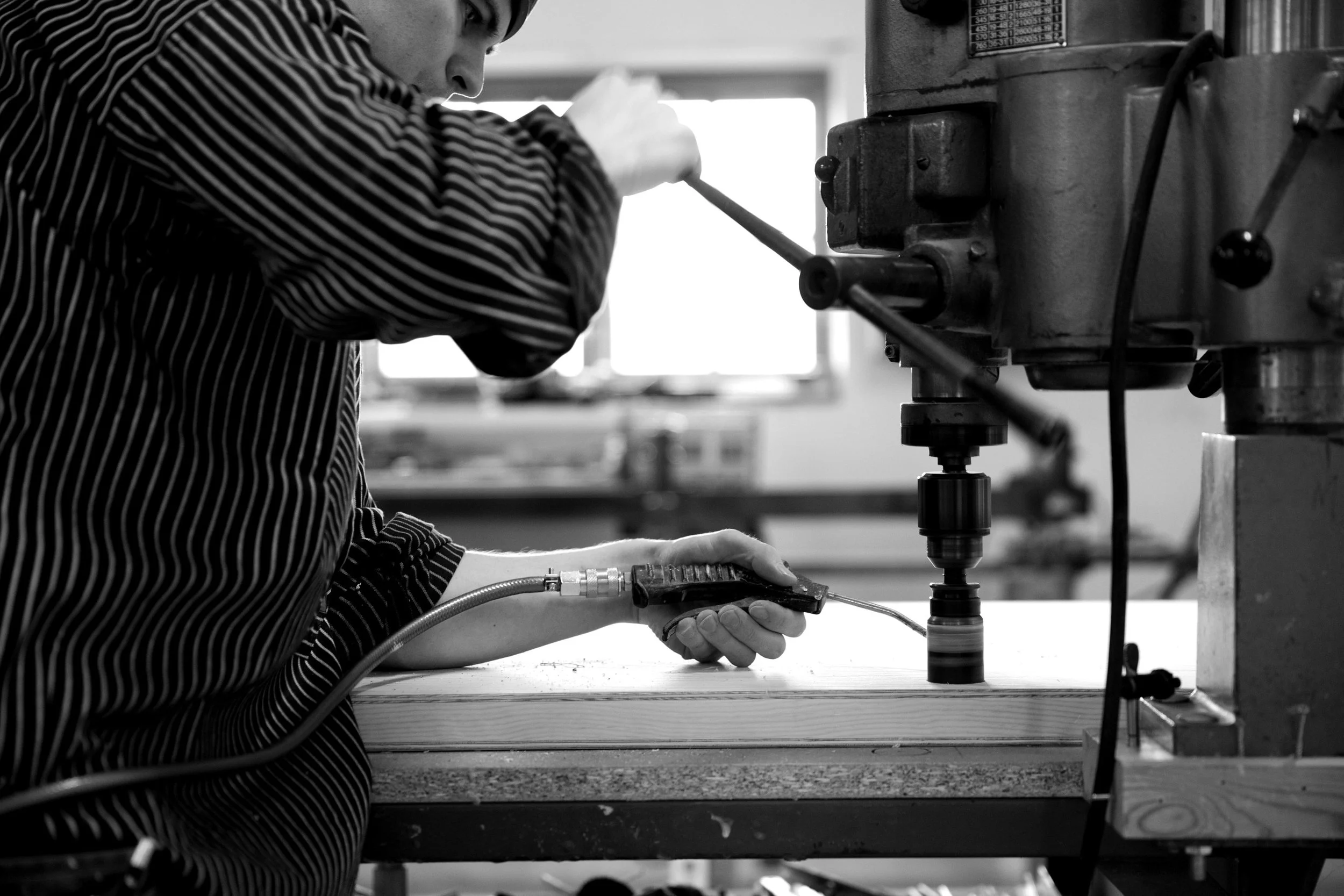 En person arbetar med en maskin i ett verkstadsmiljö, svartvitt foto.
