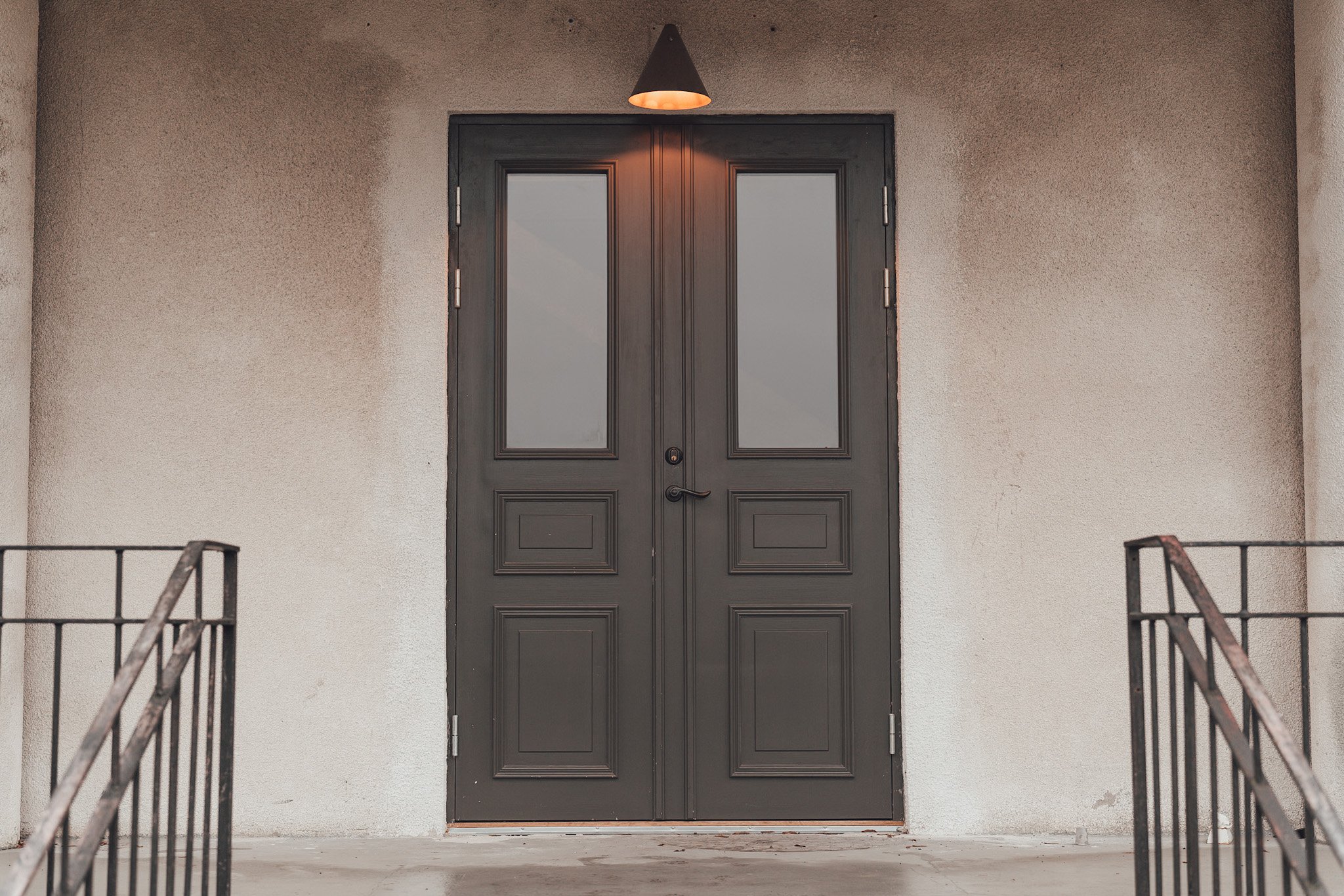 Dörr med två glasfönster, ett vägglampor ovanför, och räcken på sidorna.