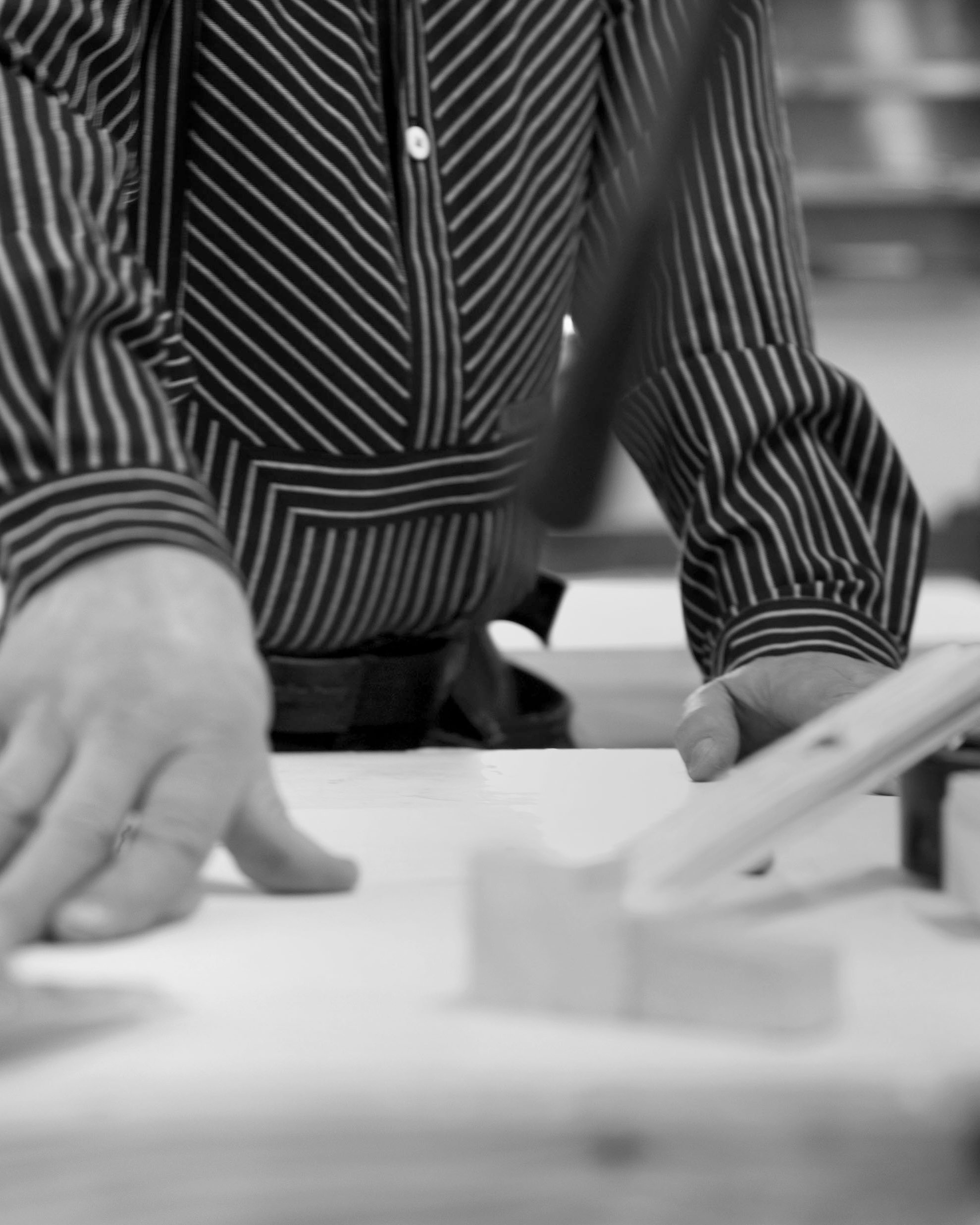 Person i svartvitt, som bär en randig skjorta, tittar på en surfplatta eller liknande device på ett bord.