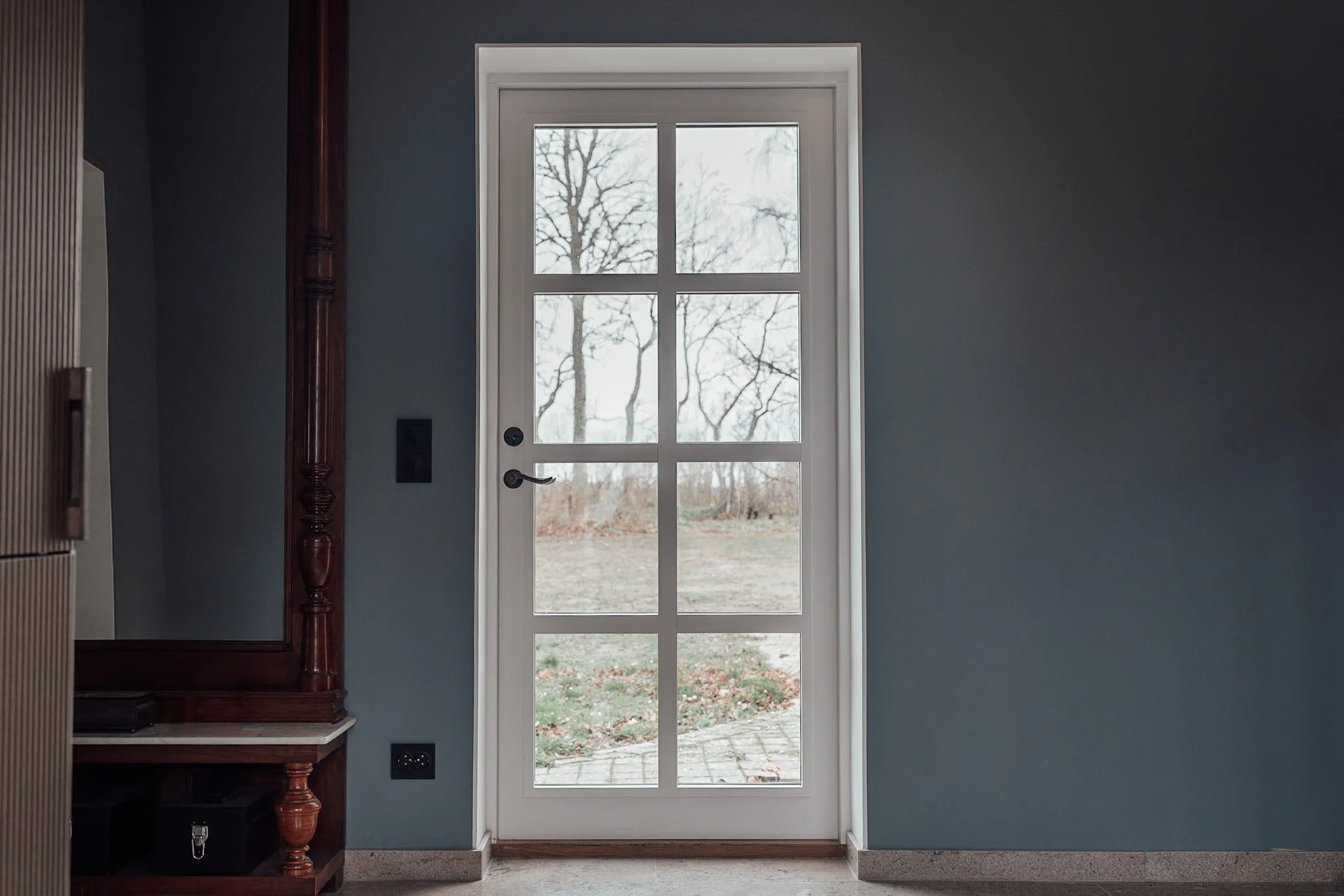 Vit fönsterdörr med sju rutor, utsikt över ett snörelt landskap med träd utomhus, i ett hem med blå väggar.