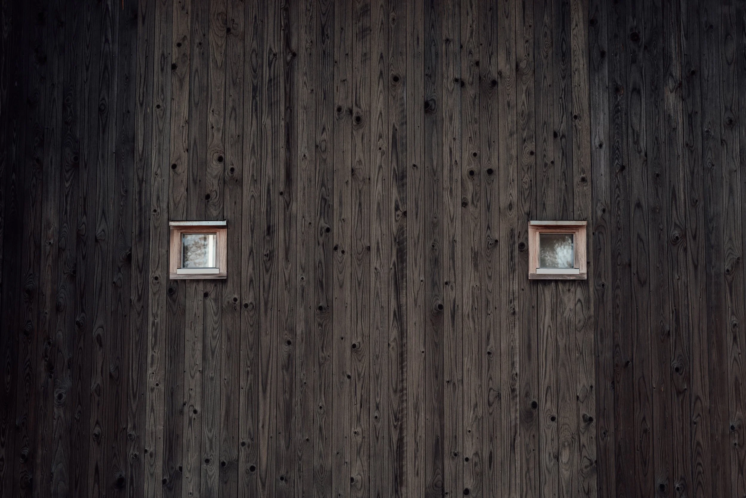 En vägg av mörkbetsad trä med två små fyrkantiga fönster.