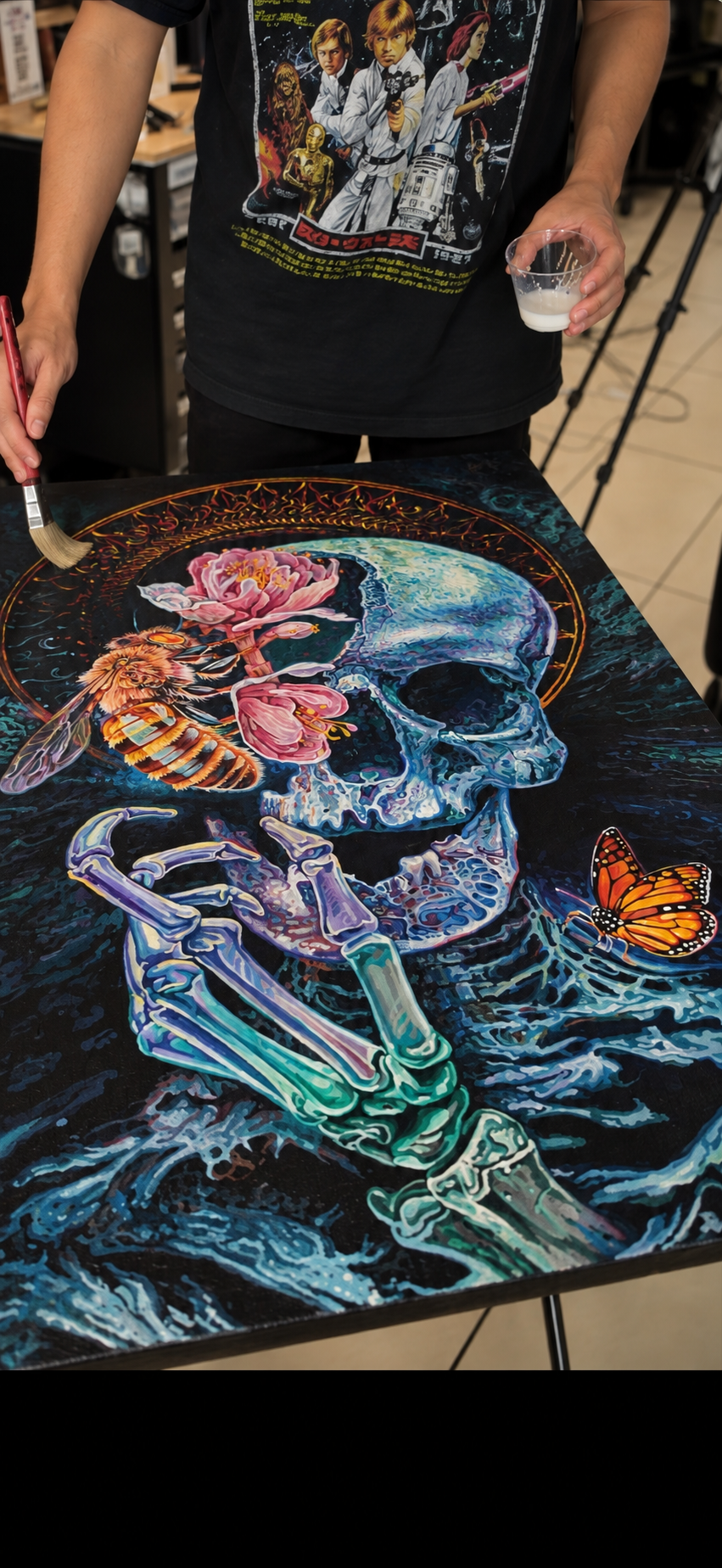 Yorlandi Fabregas applying varnish to his painting of a blue skull, flowers and a bee.