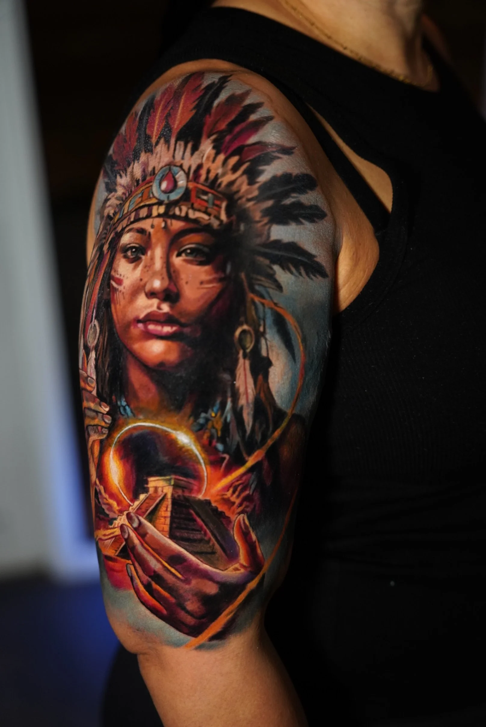 Color realism tattoo of indigenous woman with feather headdress holding a Mayan pyramid on upper arm