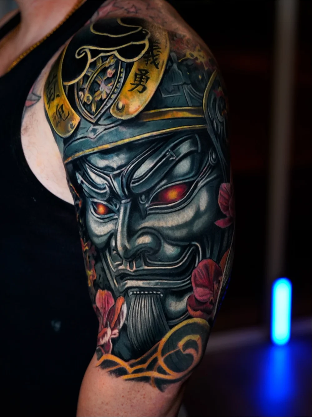 Samurai mask cover-up on the upper arm with red eyes, flowers and gold accents