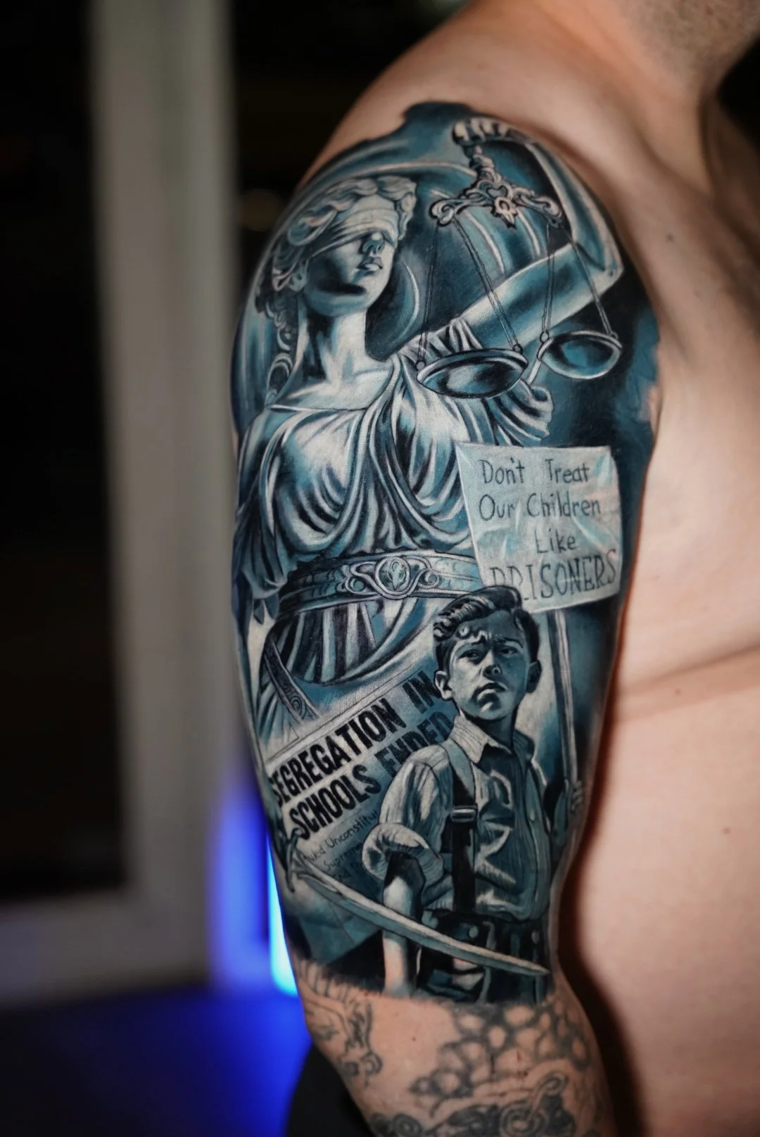 Narrative realism tattoo combining classical symbolism with social commentary. This section of the sleeve balances contrast, composition, and layered meaning within a large-scale custom tattoo.