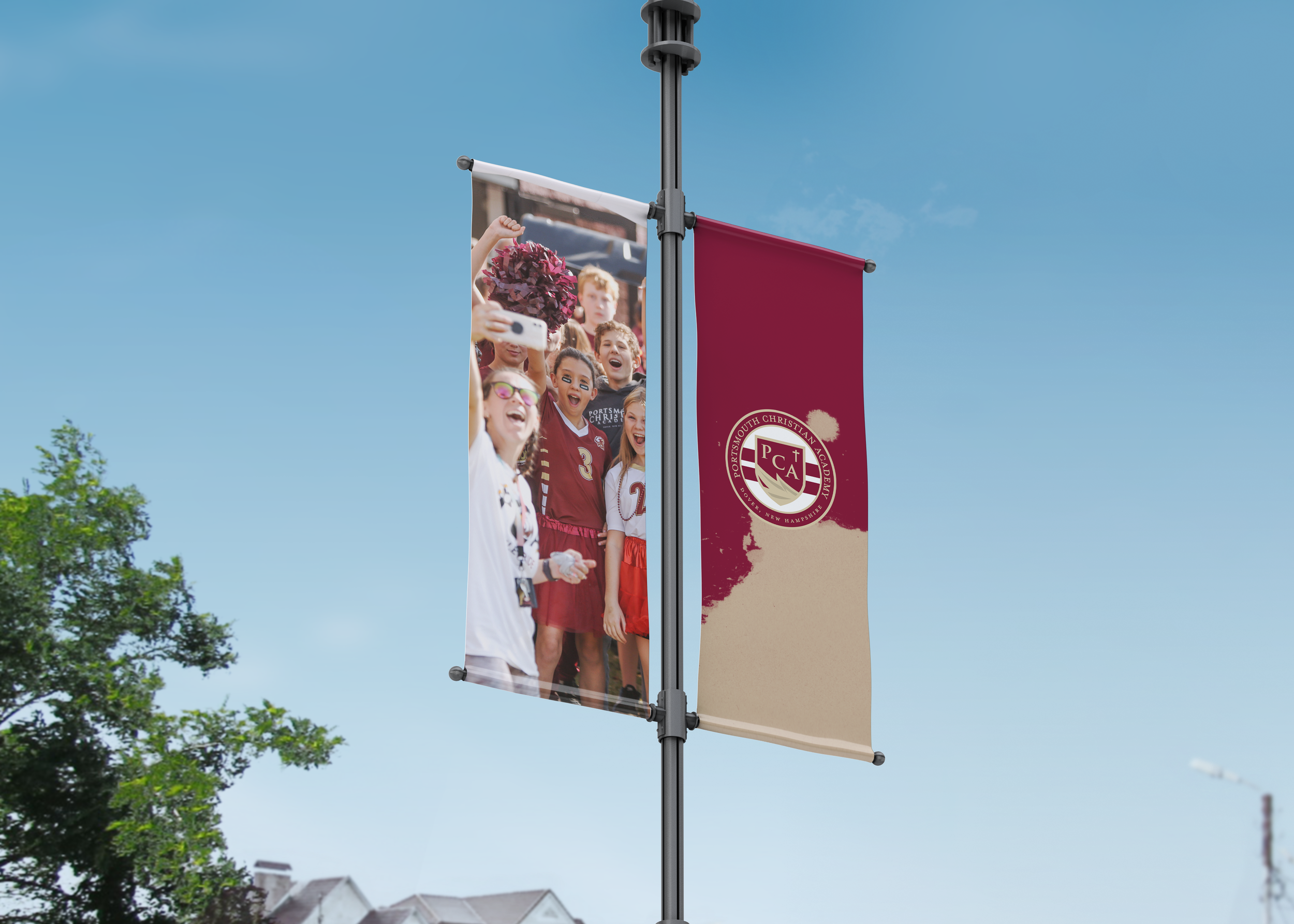 Flag featuring a group of children at a school event, some wearing sports uniforms and face paint, with a school emblem from Portsmouth Christian Academy on the flag against a blue sky.