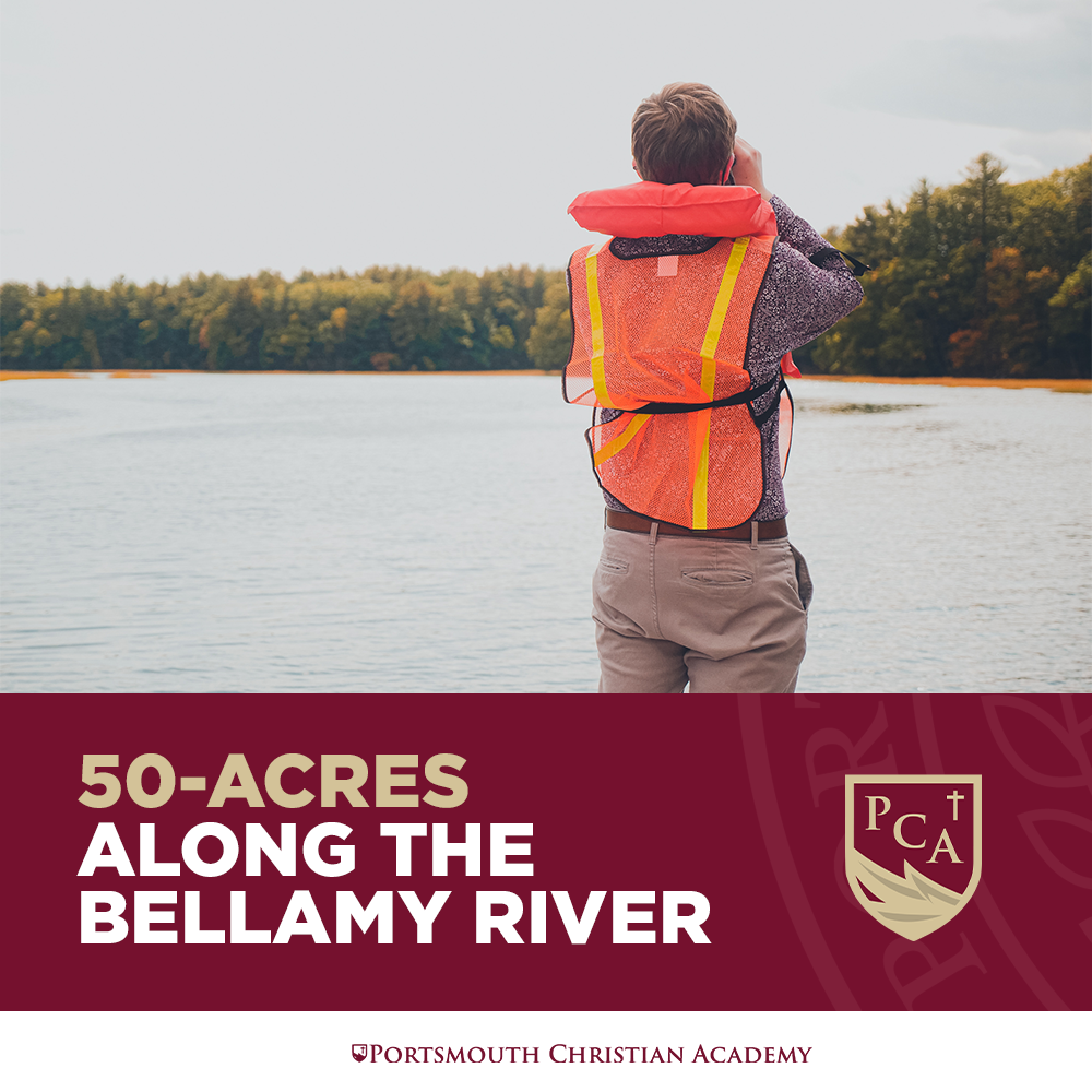 A young boy wearing a life jacket, standing by a river and looking through binoculars at the water.