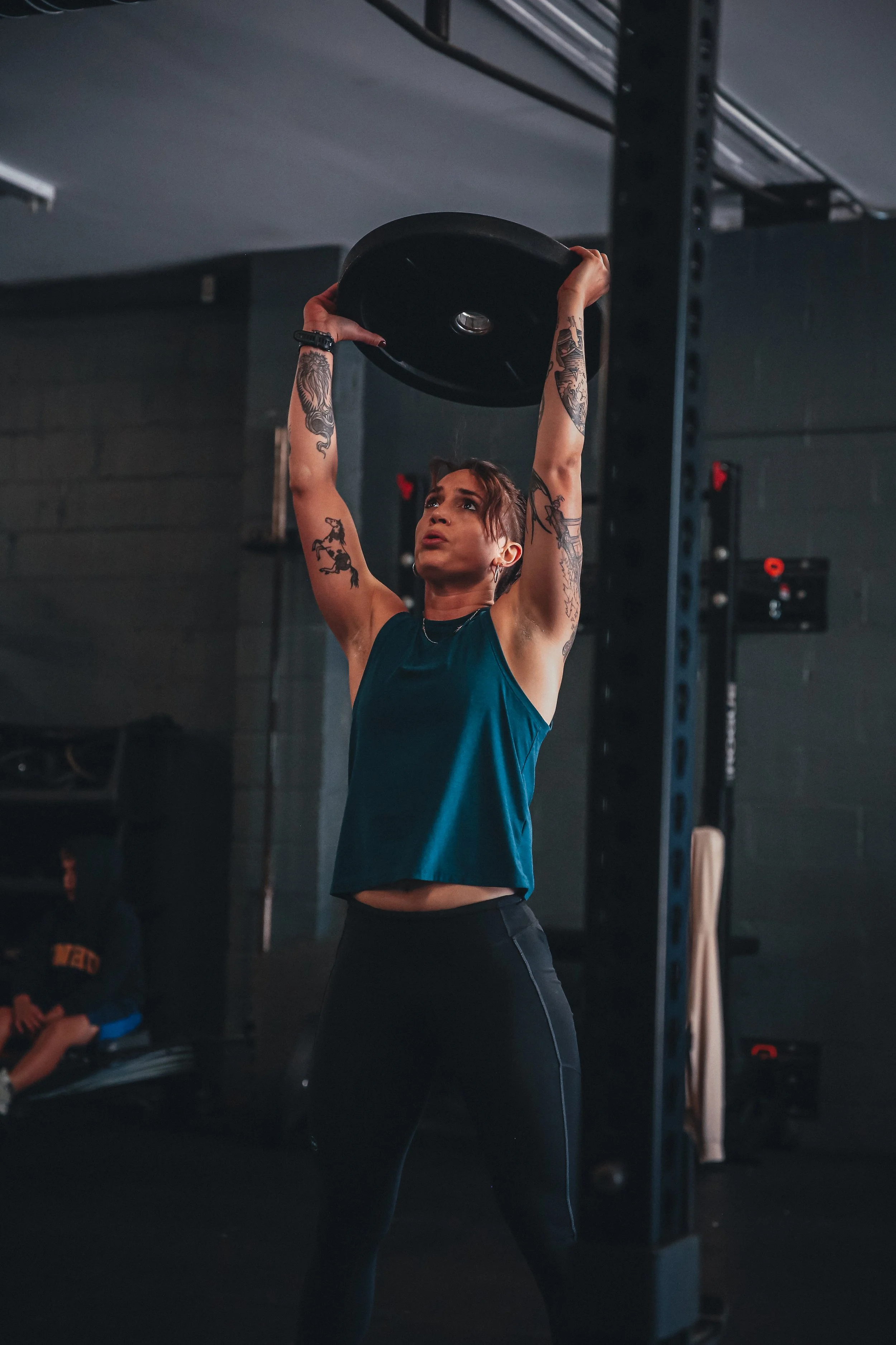 A woman lifting a weight plate overhead in a gym.