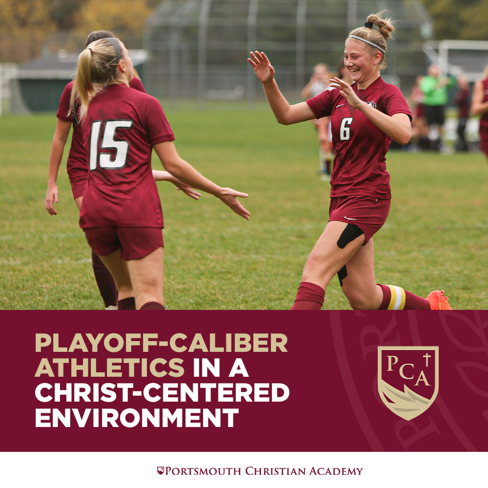Two female soccer players in maroon uniforms celebrating on the field, with one giving a high-five to the other, during a game.