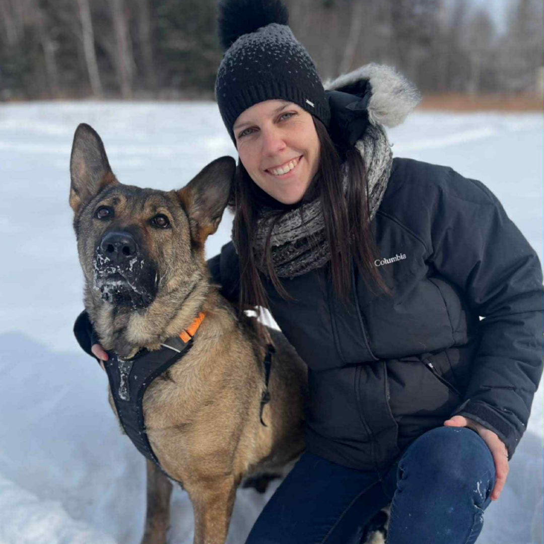 Une femme souriante avec un chien dans un paysage enneigé.
