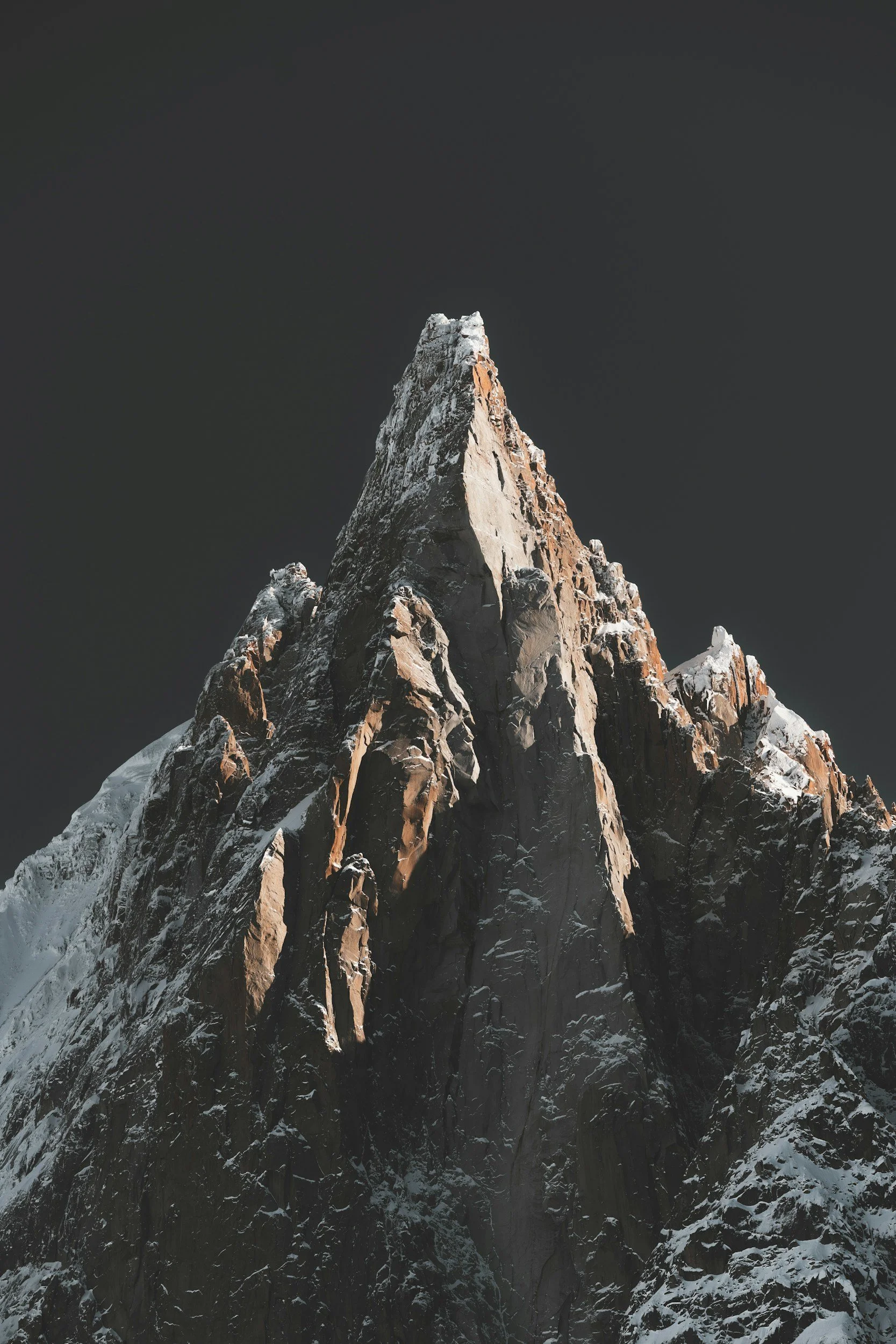A tall, snow-capped mountain peak against a dark sky.