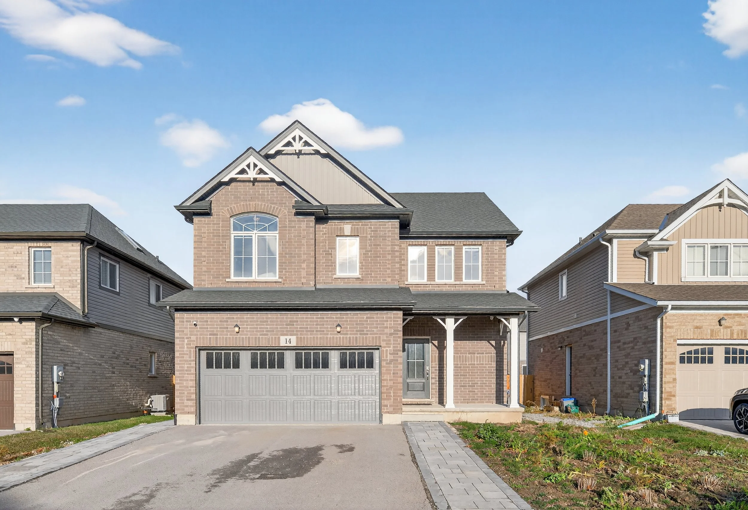A two-story brick house with a front driveway and a small porch, neighboring similar houses in a suburban neighborhood, under a partly cloudy sky.