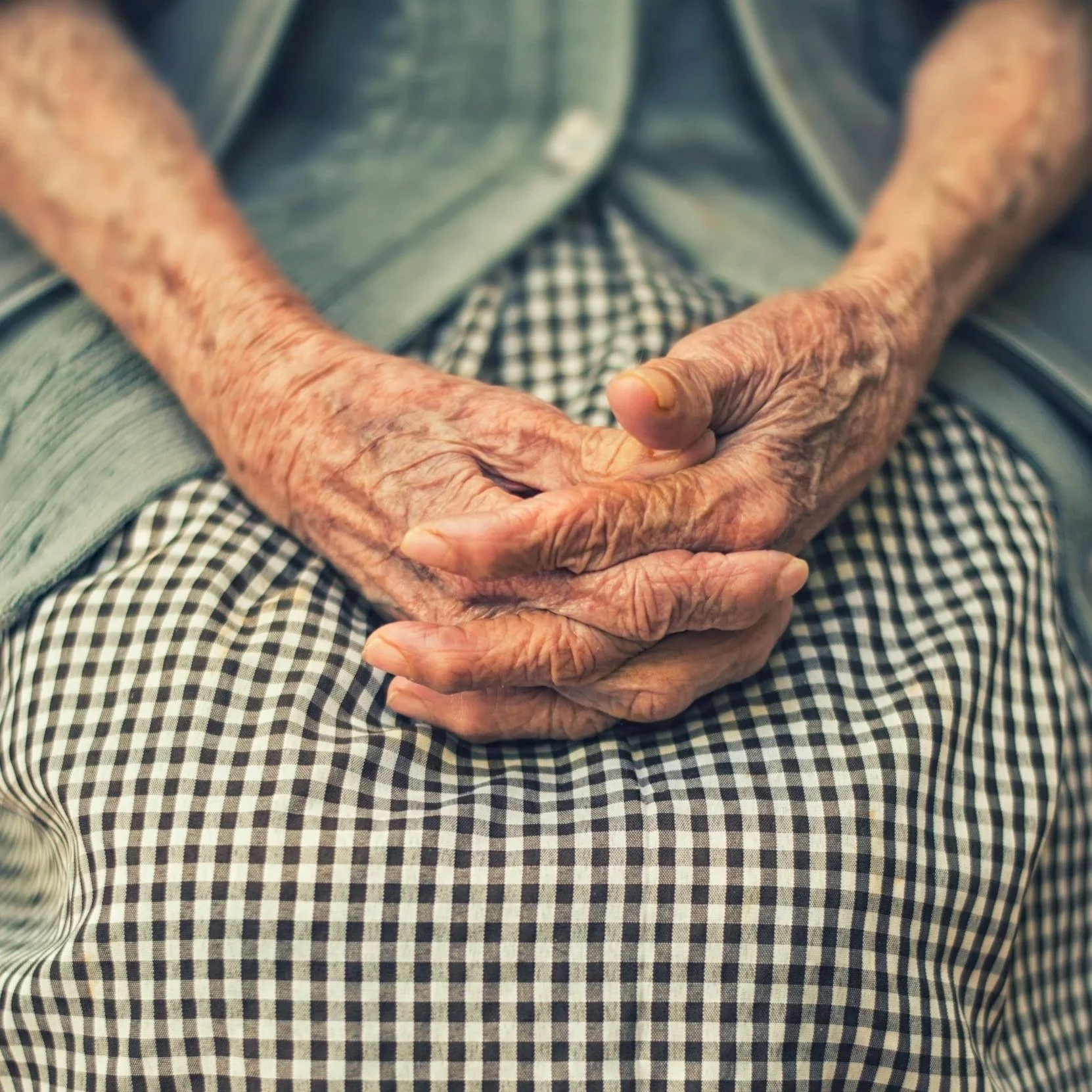 Mains d'une personne âgée reposant sur ses genoux, avec des vêtements à carreaux.