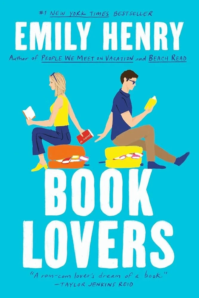Cover of the book "Book Lovers" by Emily Henry, featuring a man and a woman sitting on colorful suitcases, each reading a book, against a bright blue background. The woman has blonde hair and wears a yellow top and blue pants; the man has dark hair, sunglasses, a blue shirt, and brown pants.