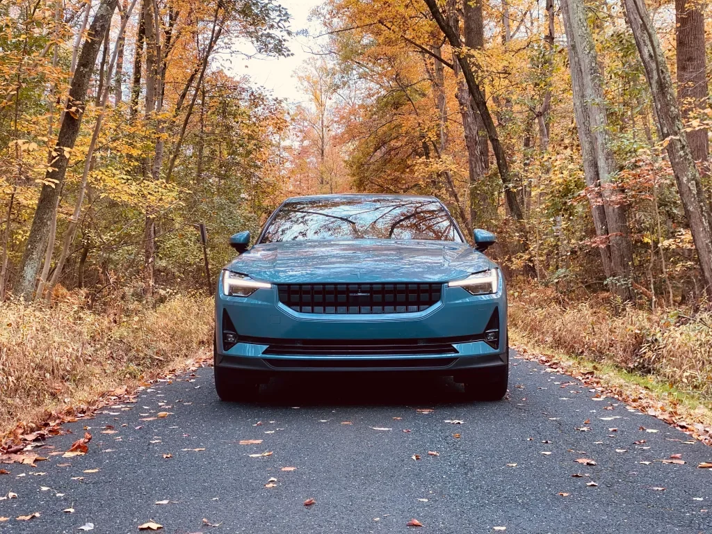 A blue car parked on a narrow road surrounded by fall-colored trees.