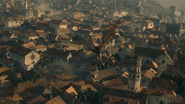 A giant dragon flying over a densely packed town with many rooftops and a prominent tower.