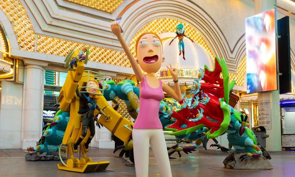 Colorful cartoon sculptures of a woman with glasses, surrounded by various animated characters, outside a brightly lit building.