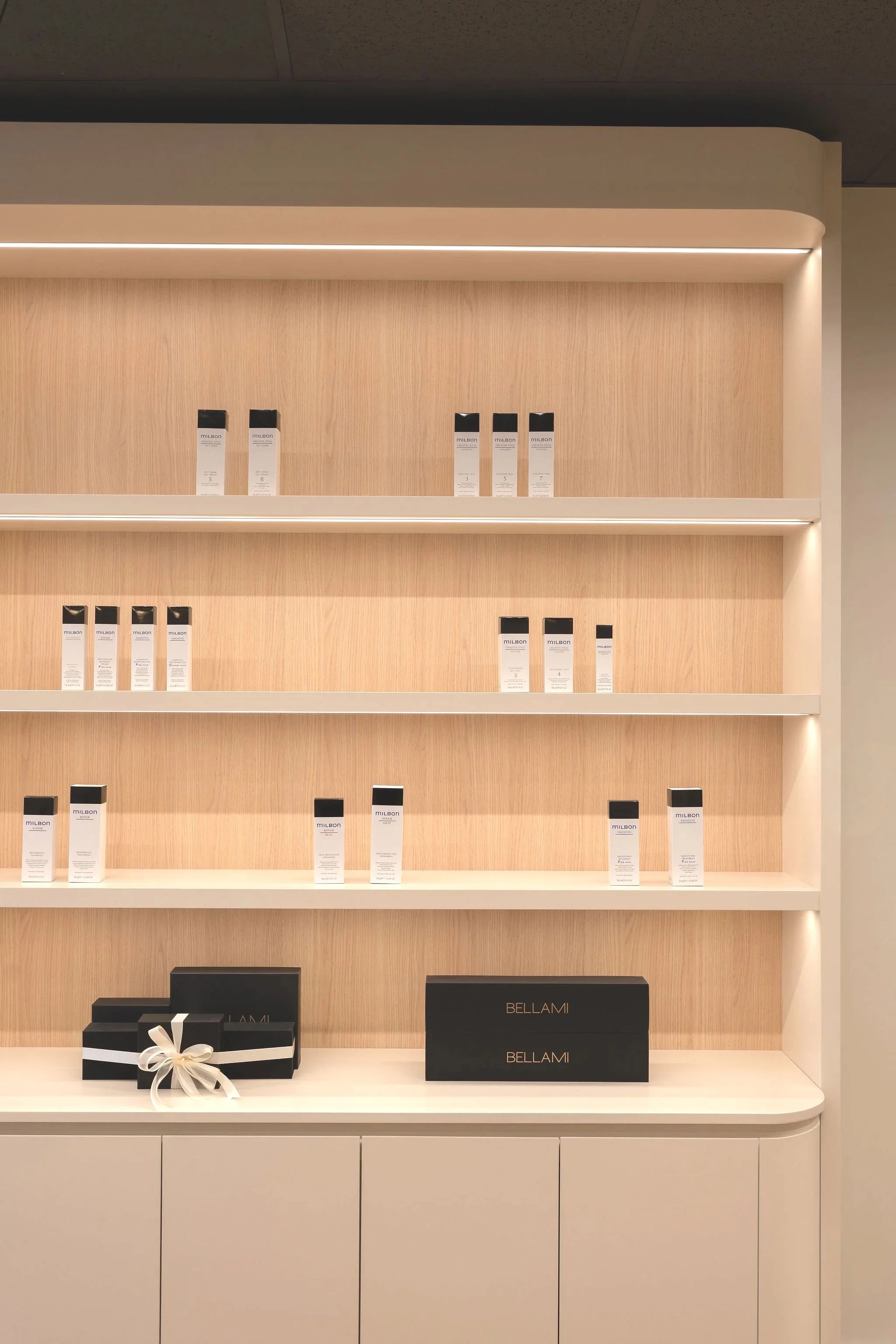 Display shelf with multiple bottles of skincare or cosmetic products and two black boxes labeled 'BELLAMI' on a light-colored cabinet.