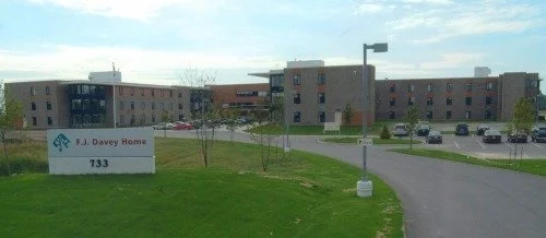 The image shows an apartment complex with a parking lot and grassy area in front. A sign reads 'F.J. Davey Home, 733'.