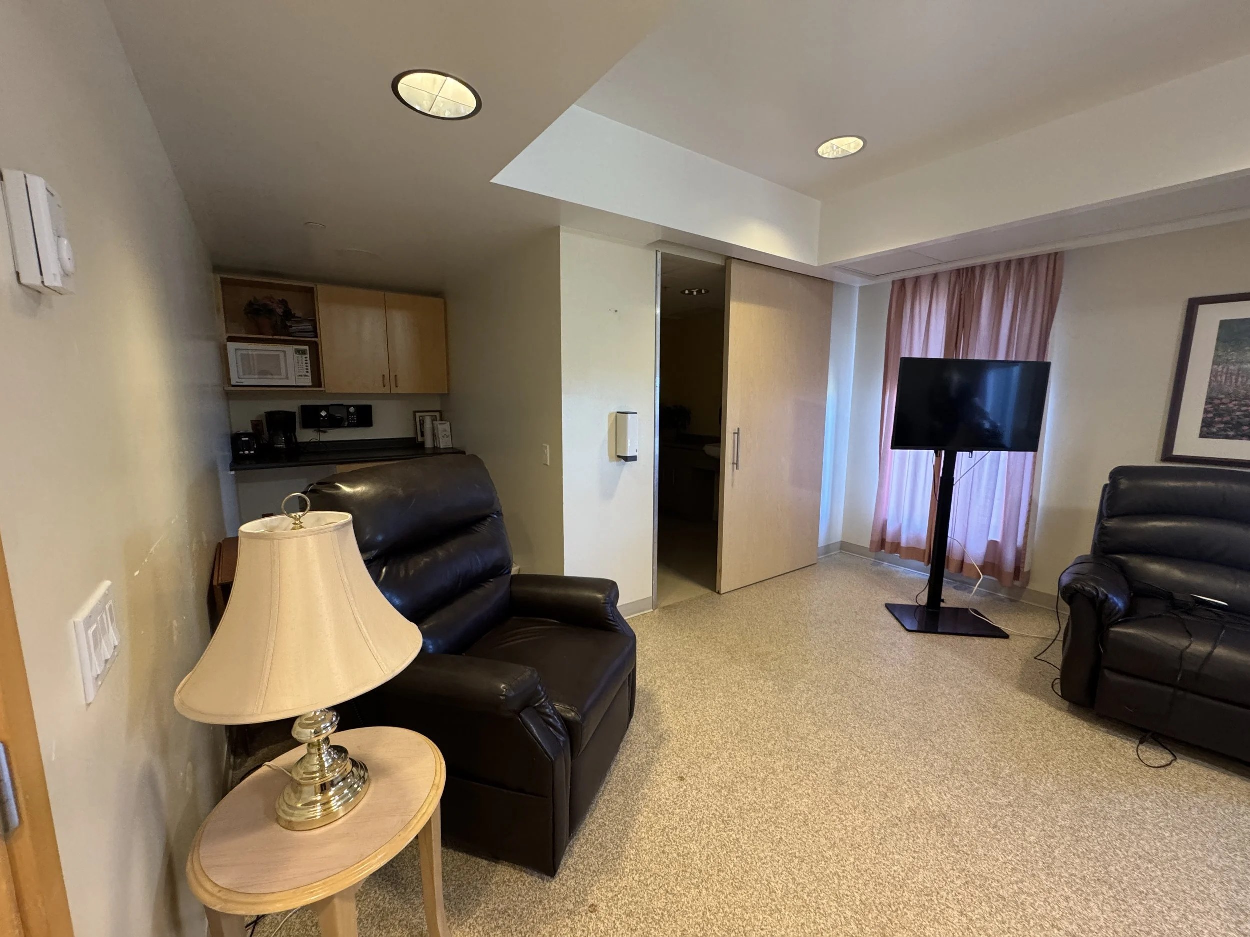 Serenity Room: The room features comfortable reclining chairs where family members can rest and stay close to their loved one, as well as a TV for relaxation and companionship. An attached washroom provides convenience and privacy, while the small ki