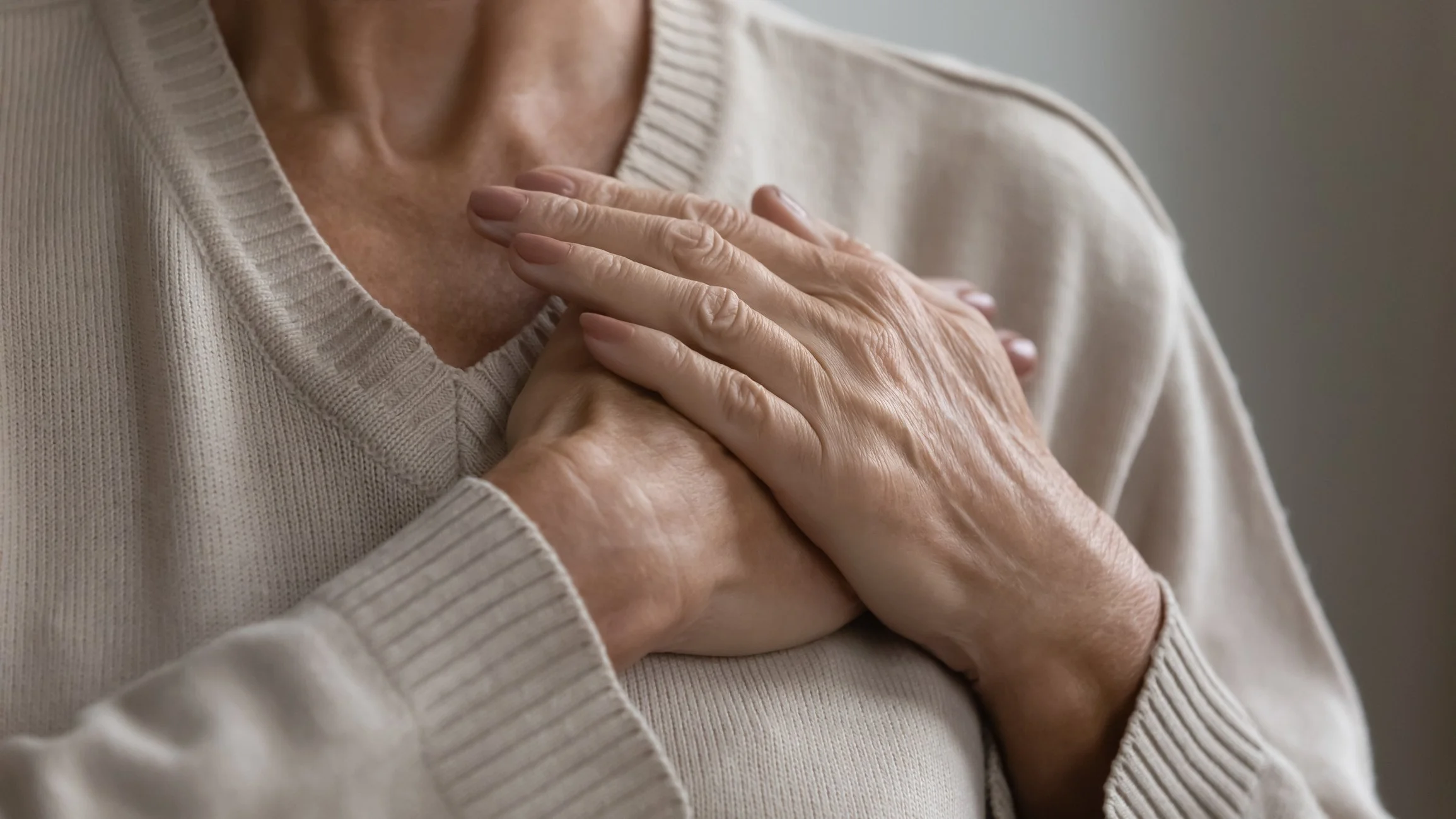An elderly person placing one hand over their chest, showing vulnerability and emotion.