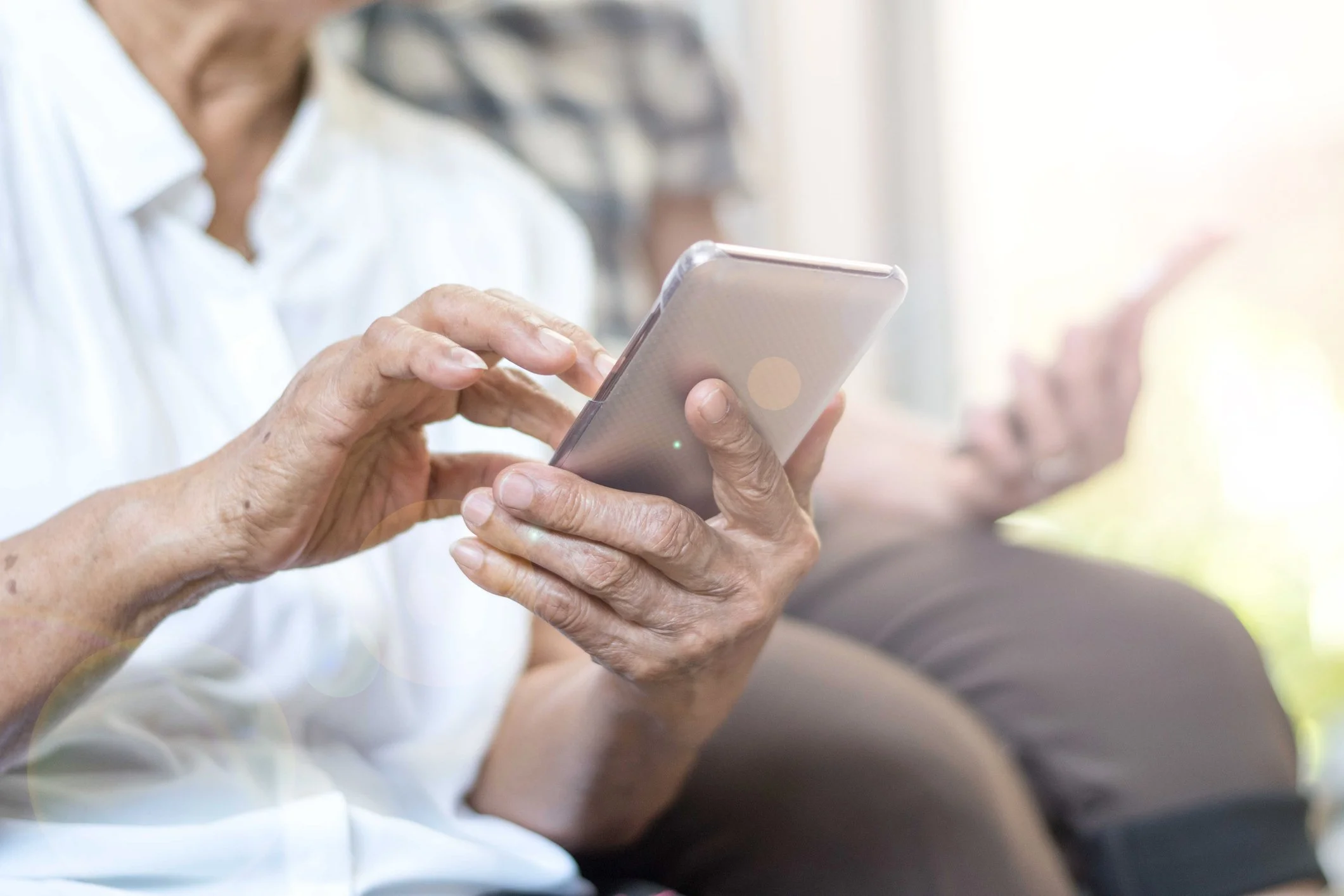 Close-up of elderly woman using a smartphone, with focus on her hands and phone, and blurred background.
